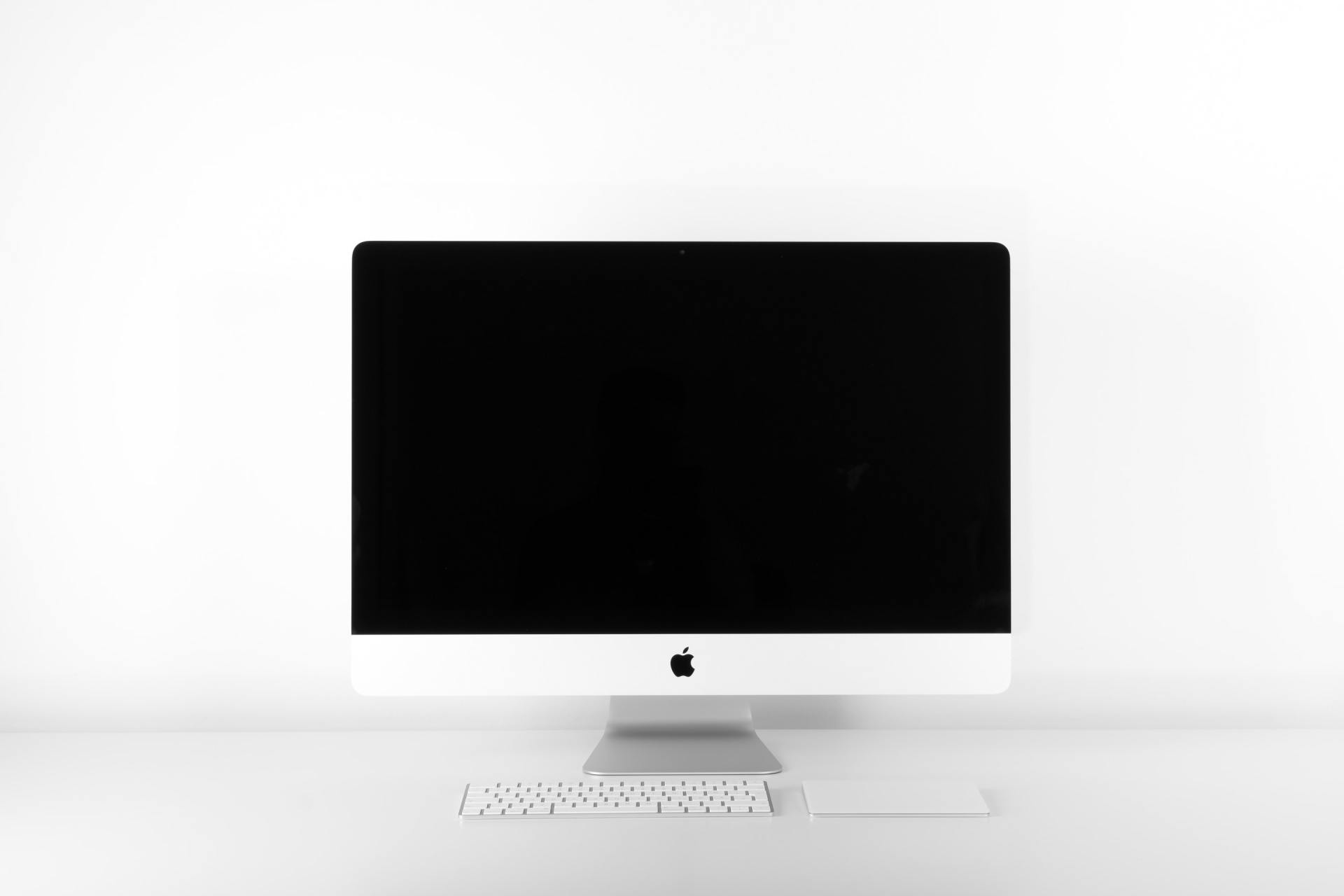 An Apple iMac computer with a keyboard and trackpad sitting on a clean, white desk against a white background.