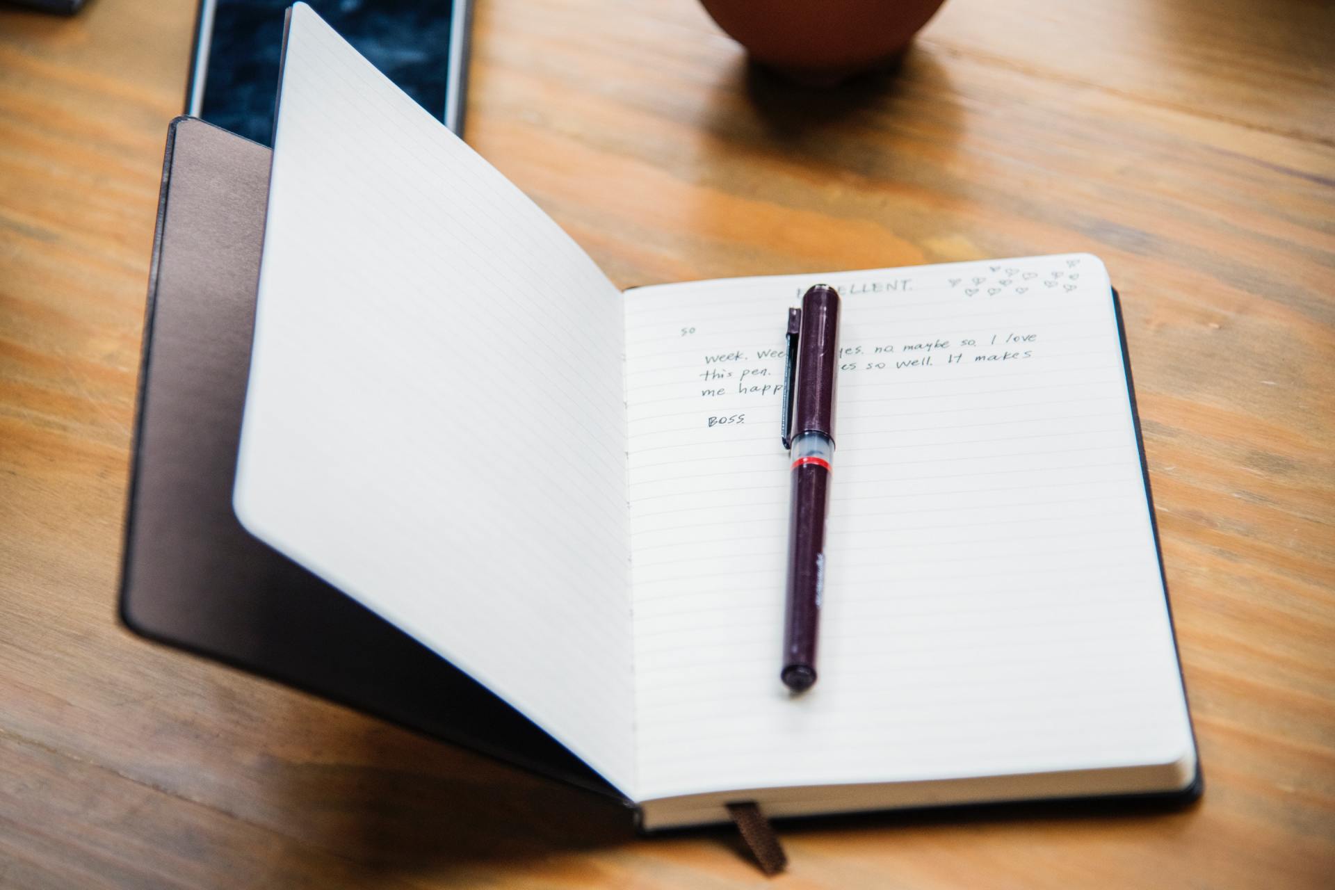 A pen is sitting on top of an open notebook on a wooden table.