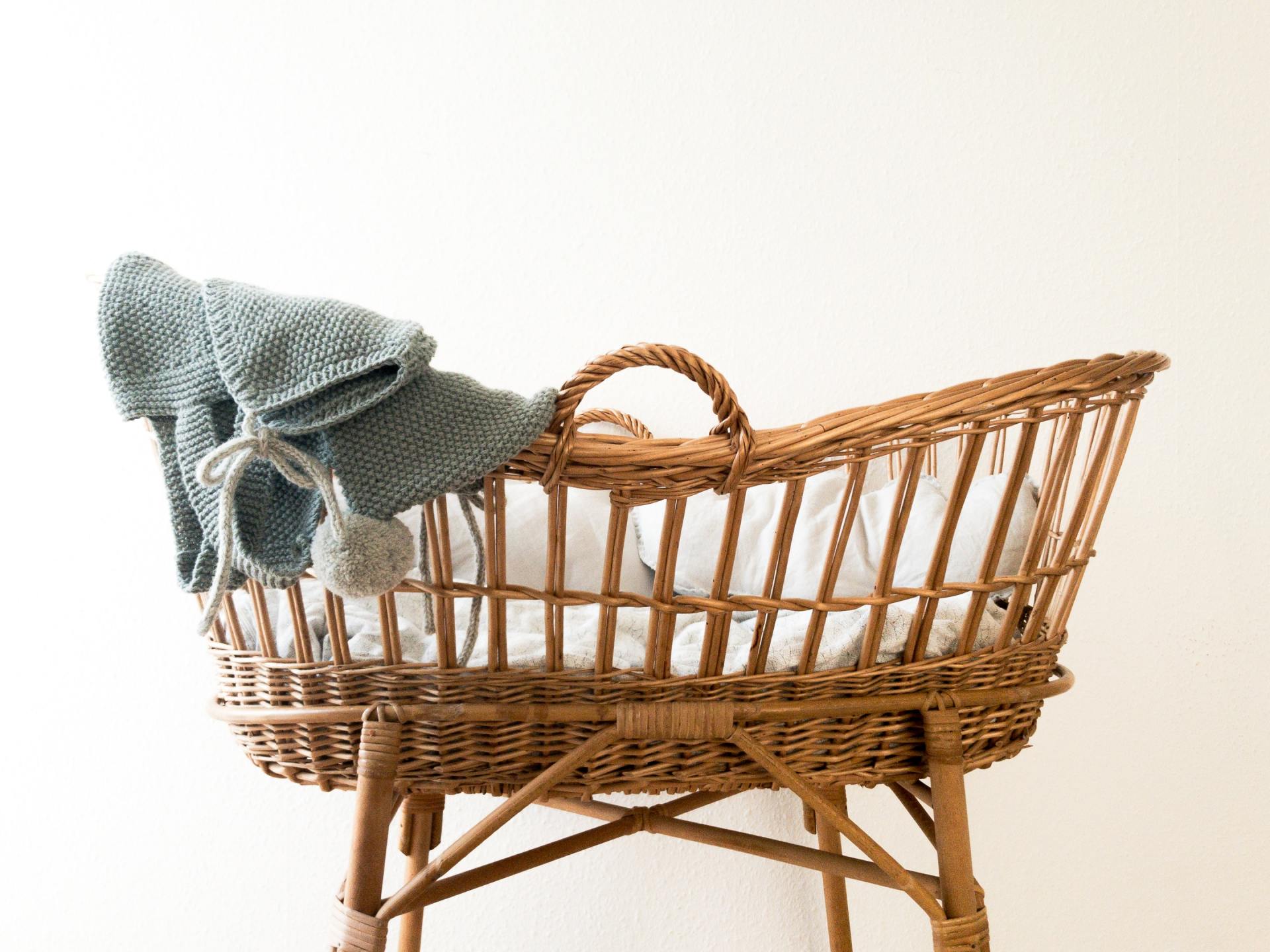 A photo of a wicker bassinet with a knit blanket draped over the side