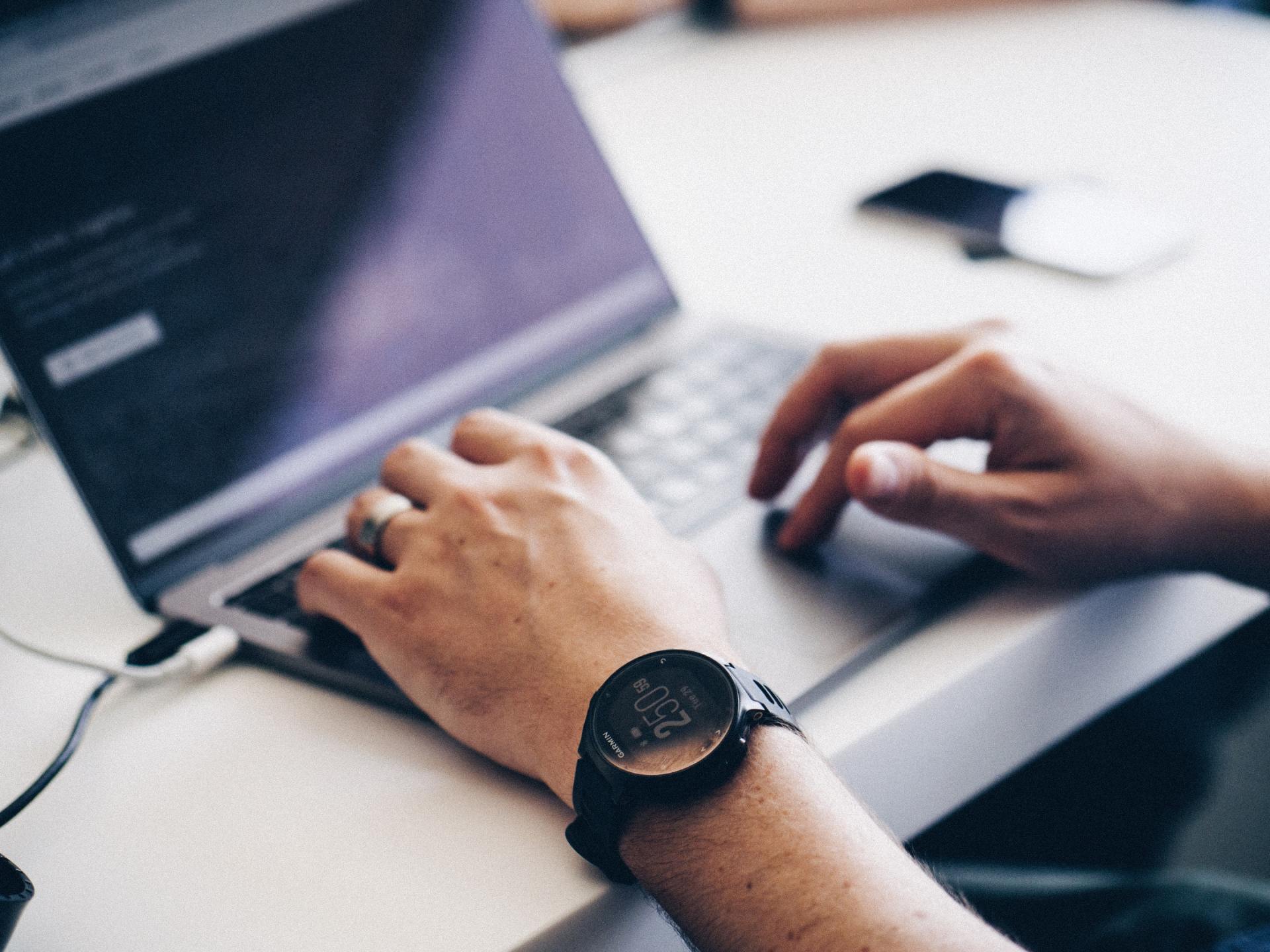 A person wearing a watch is typing on a laptop