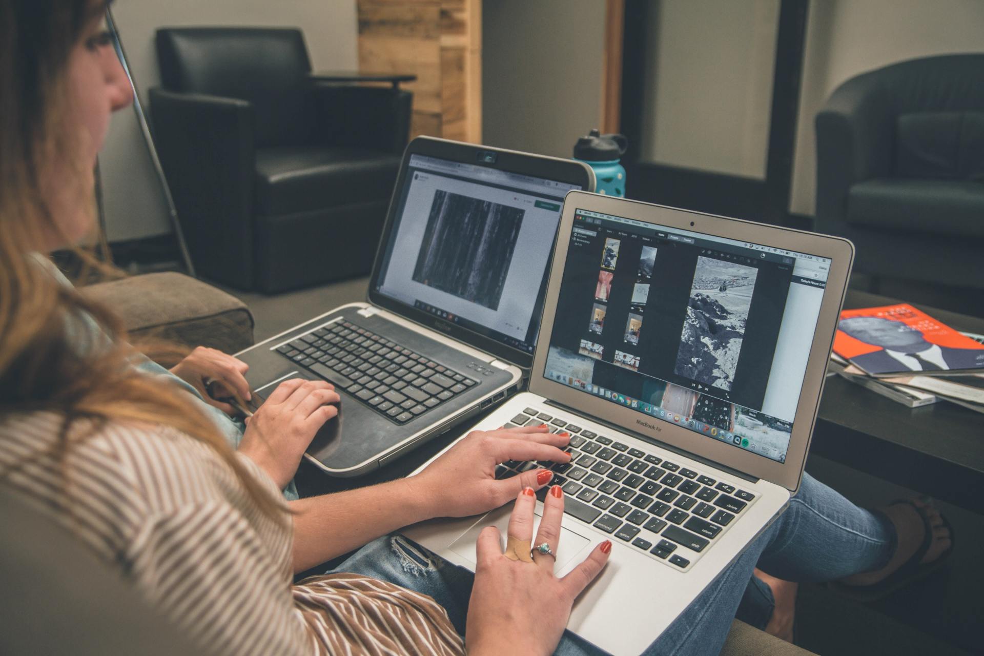 A woman is sitting on a couch using two laptops.