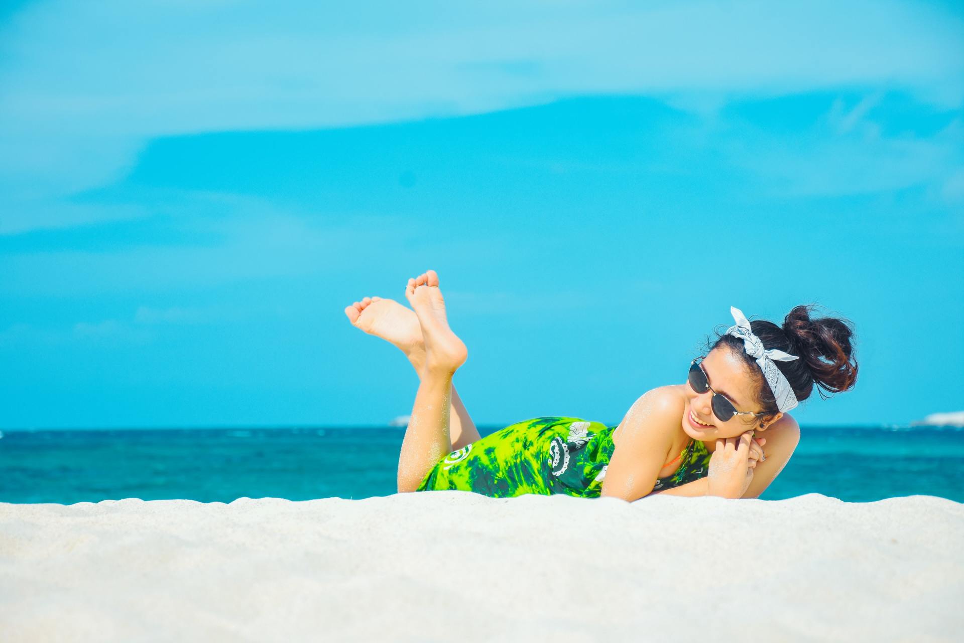 A woman with sunglasses is laying on her stomach on the beach