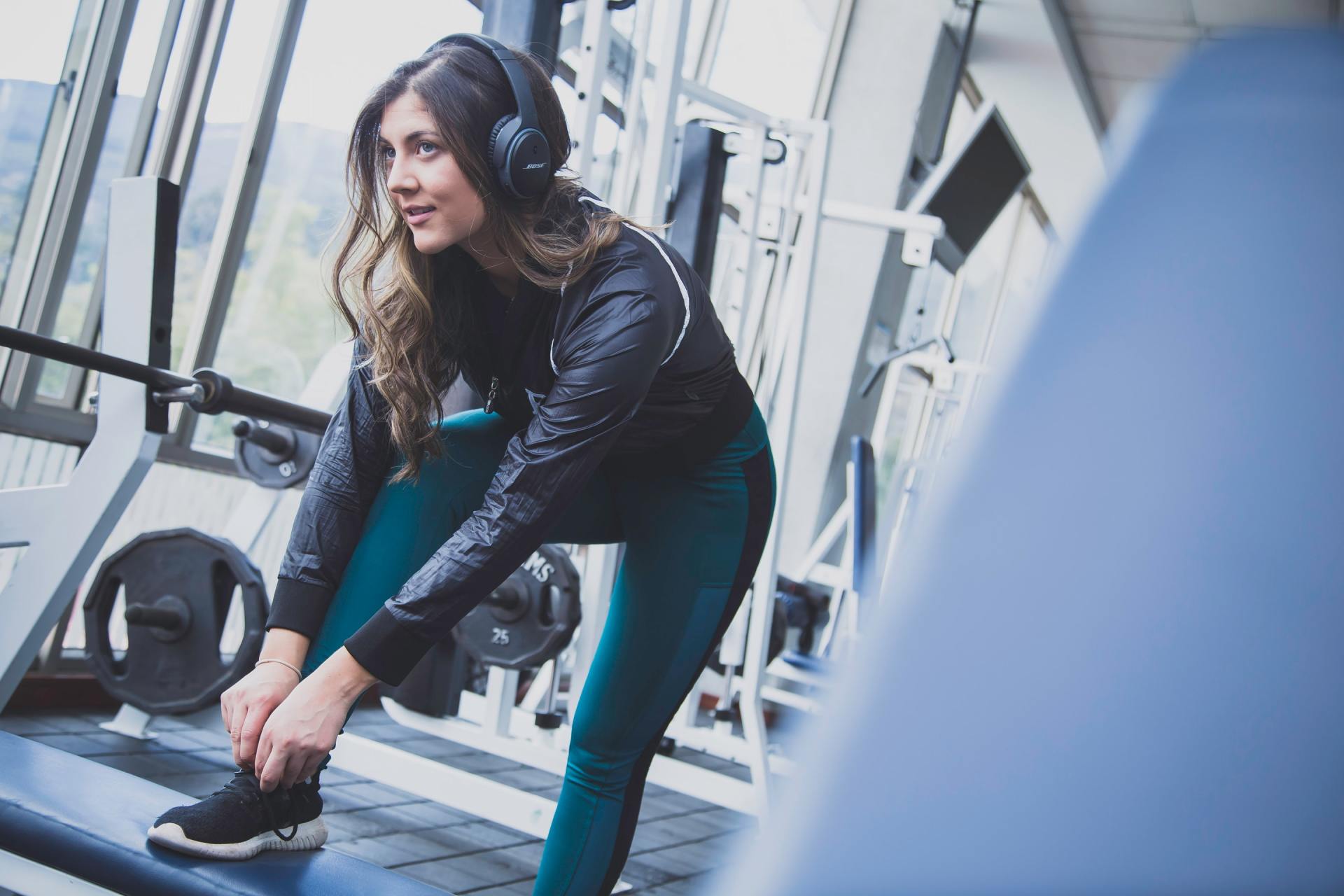 Woman in gym tying shoe, wearing headphones and workout clothes.