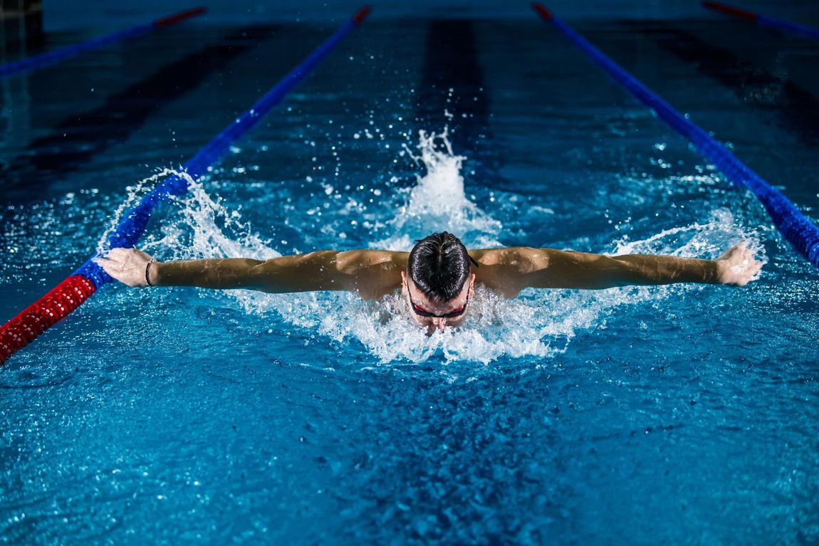 A man is swimming in a swimming pool in a butterfly stroke.
