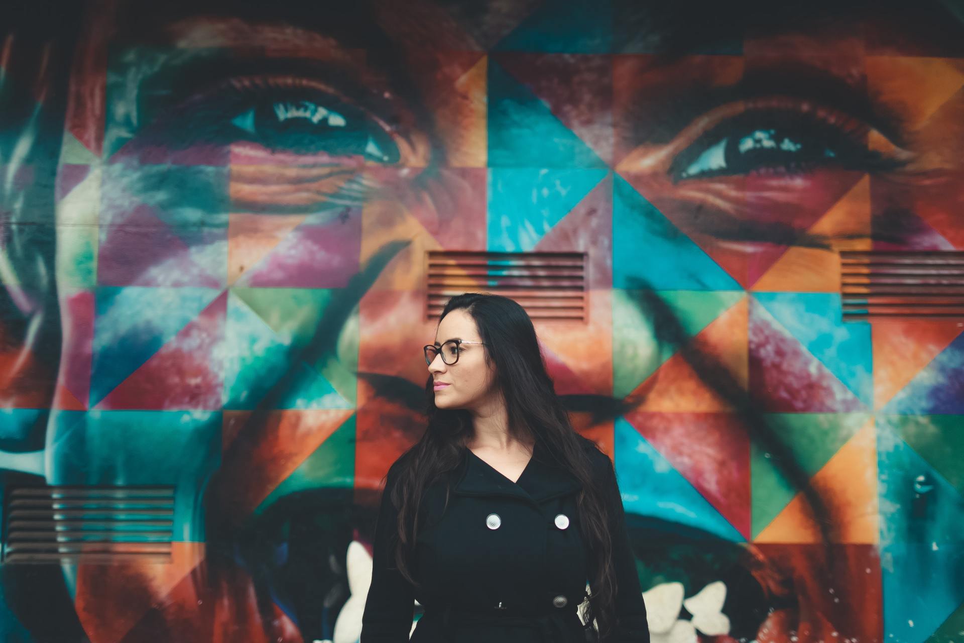 Uma mulher está parada em frente a um mural colorido de um rosto.