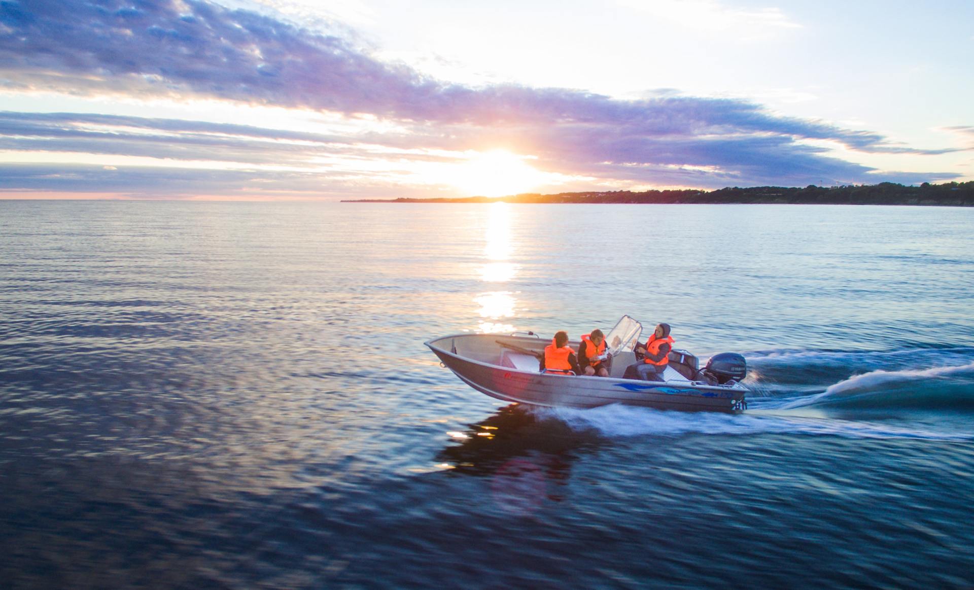 Menschen fahren bei Sonnenuntergang mit einem kleinen Motorboot auf ruhigem Meer, das Wasser glänzt in goldenem Licht.