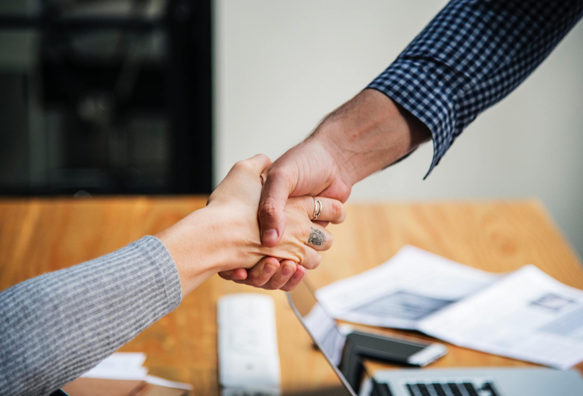 Hands clasping in a business meeting over a table with papers and a laptop.