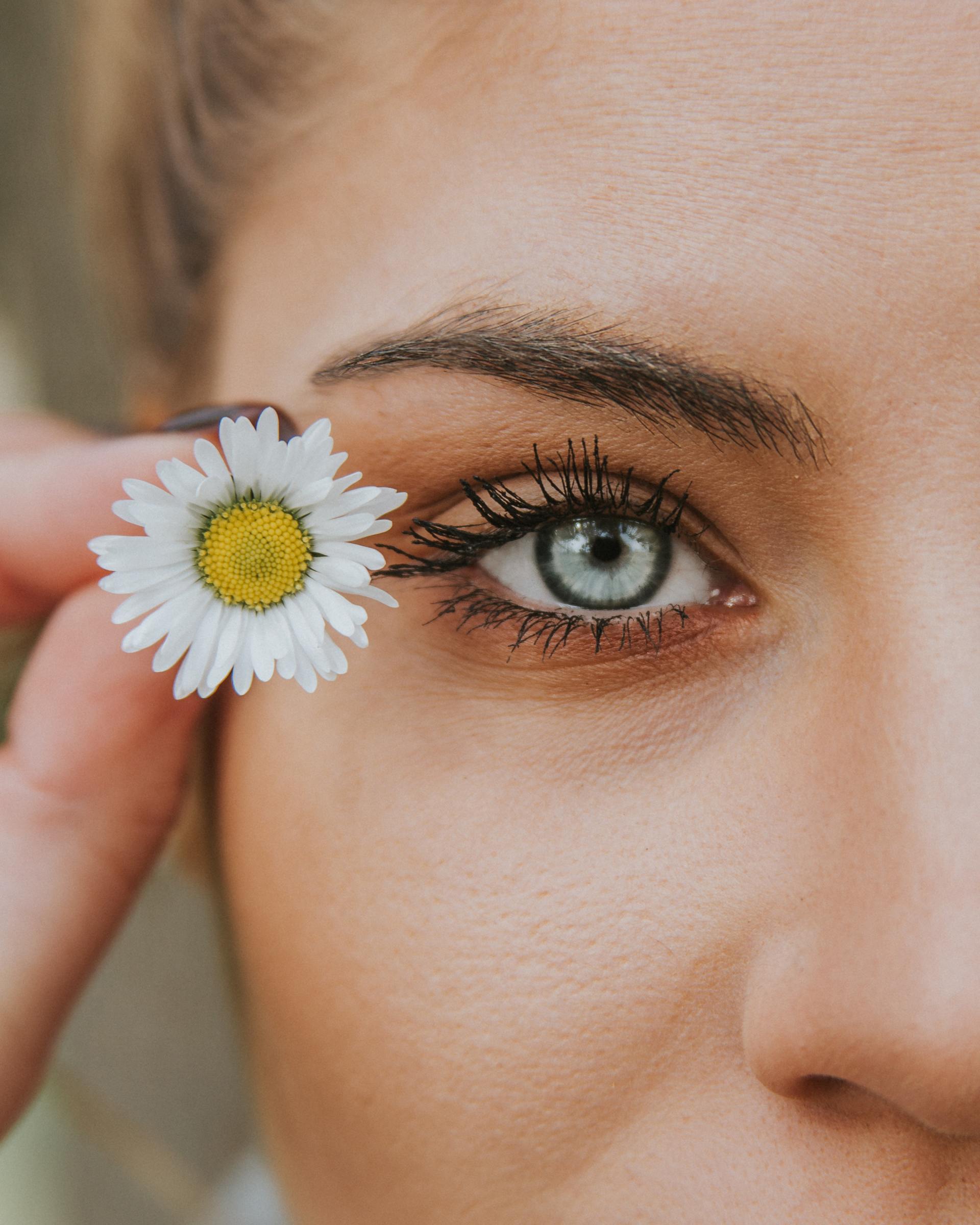 A woman is holding a flower in front of her eye.