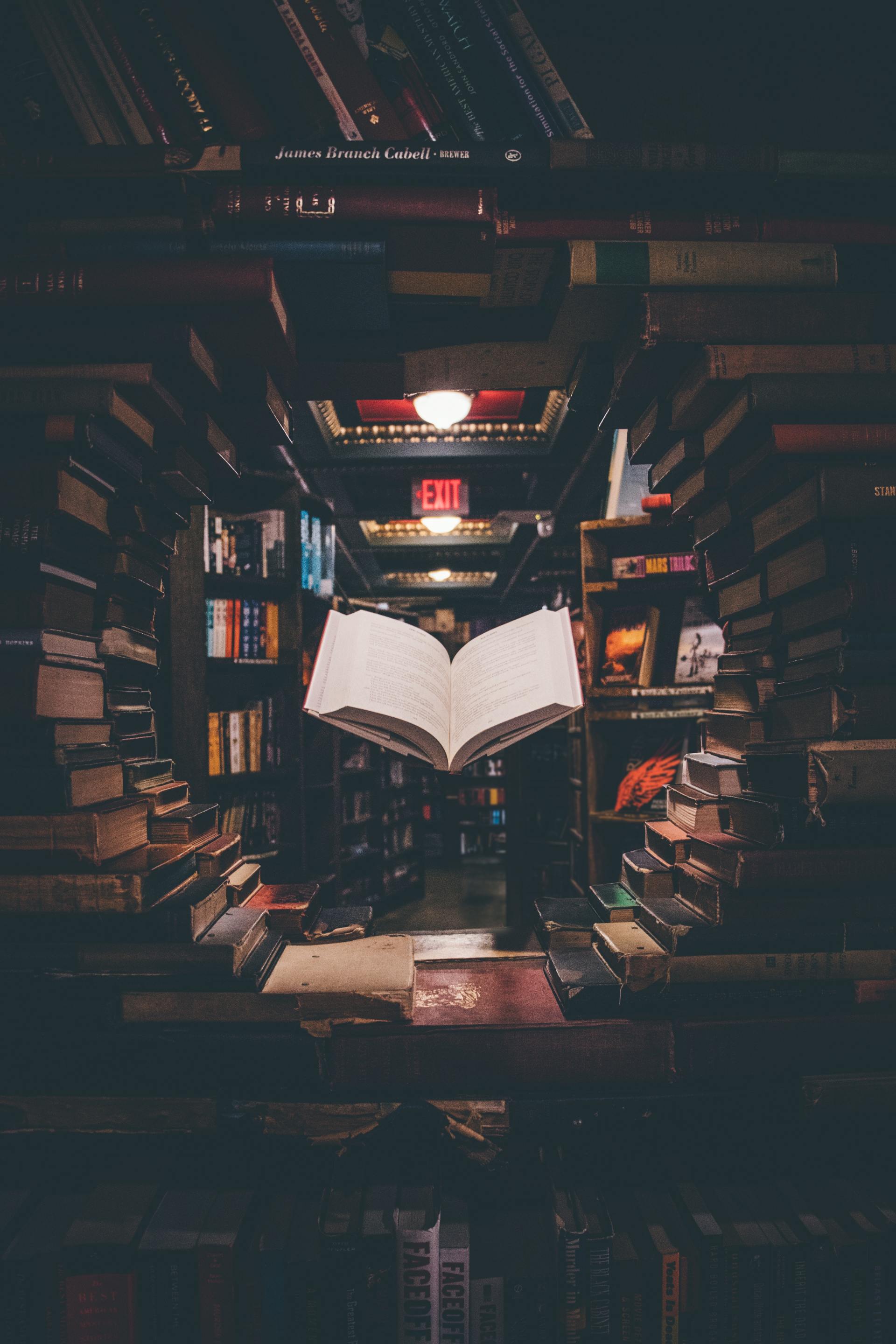 An open book is sitting on a table in a library surrounded by books.
