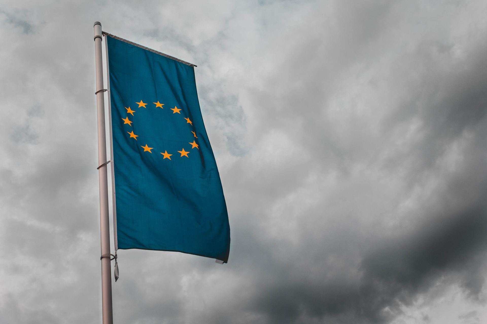 EU flag with yellow stars is waving in the wind against a cloudy sky.