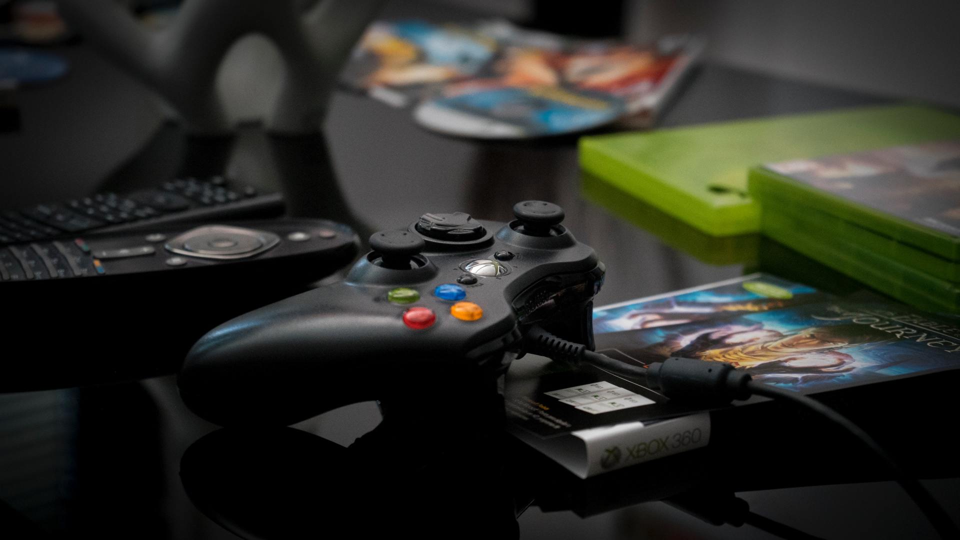 A video game controller is sitting on top of a stack of video games.