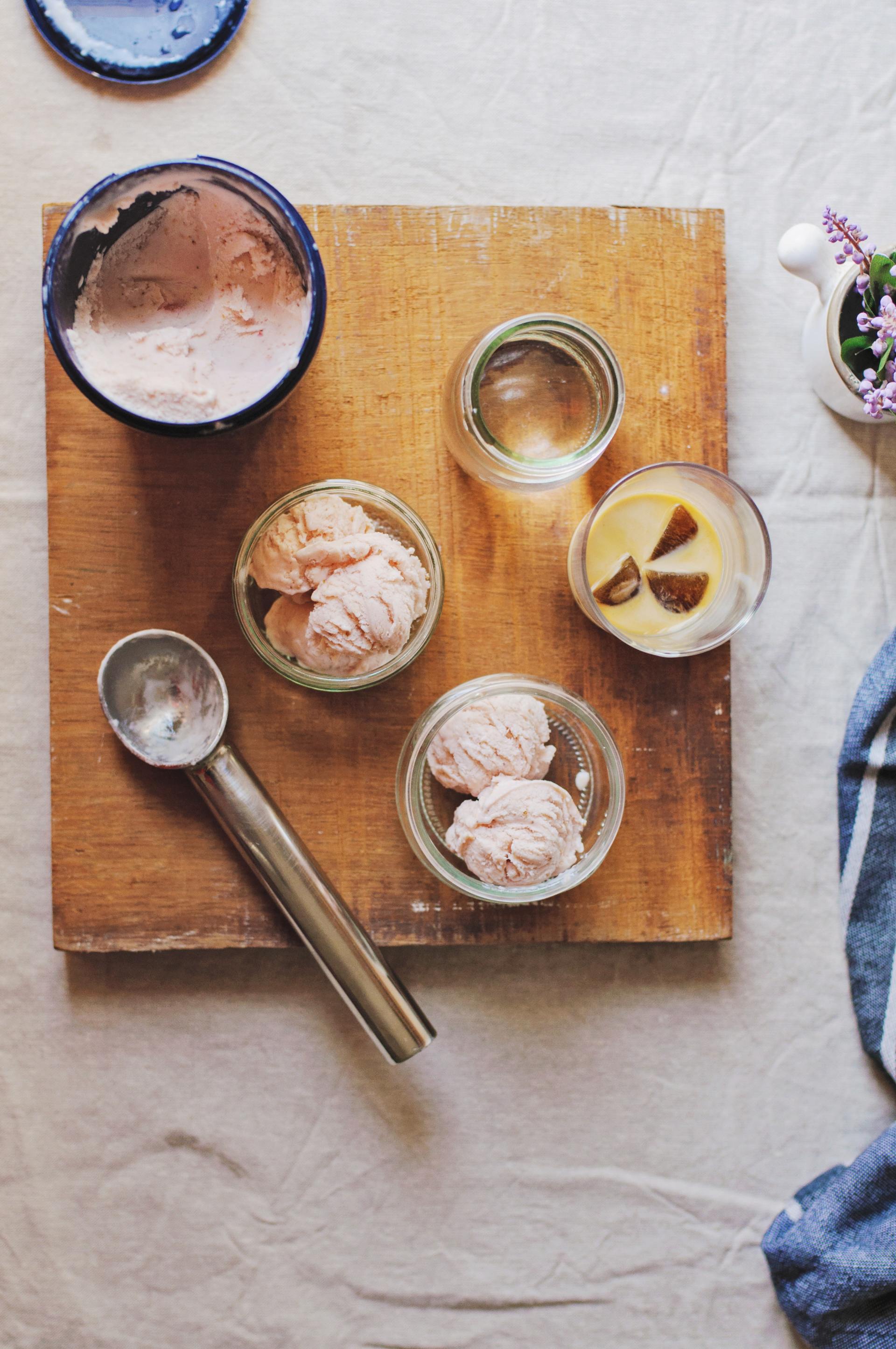 Overhead view of ice cream scoops in glass dishes, an open container, and water glasses on a wooden board.