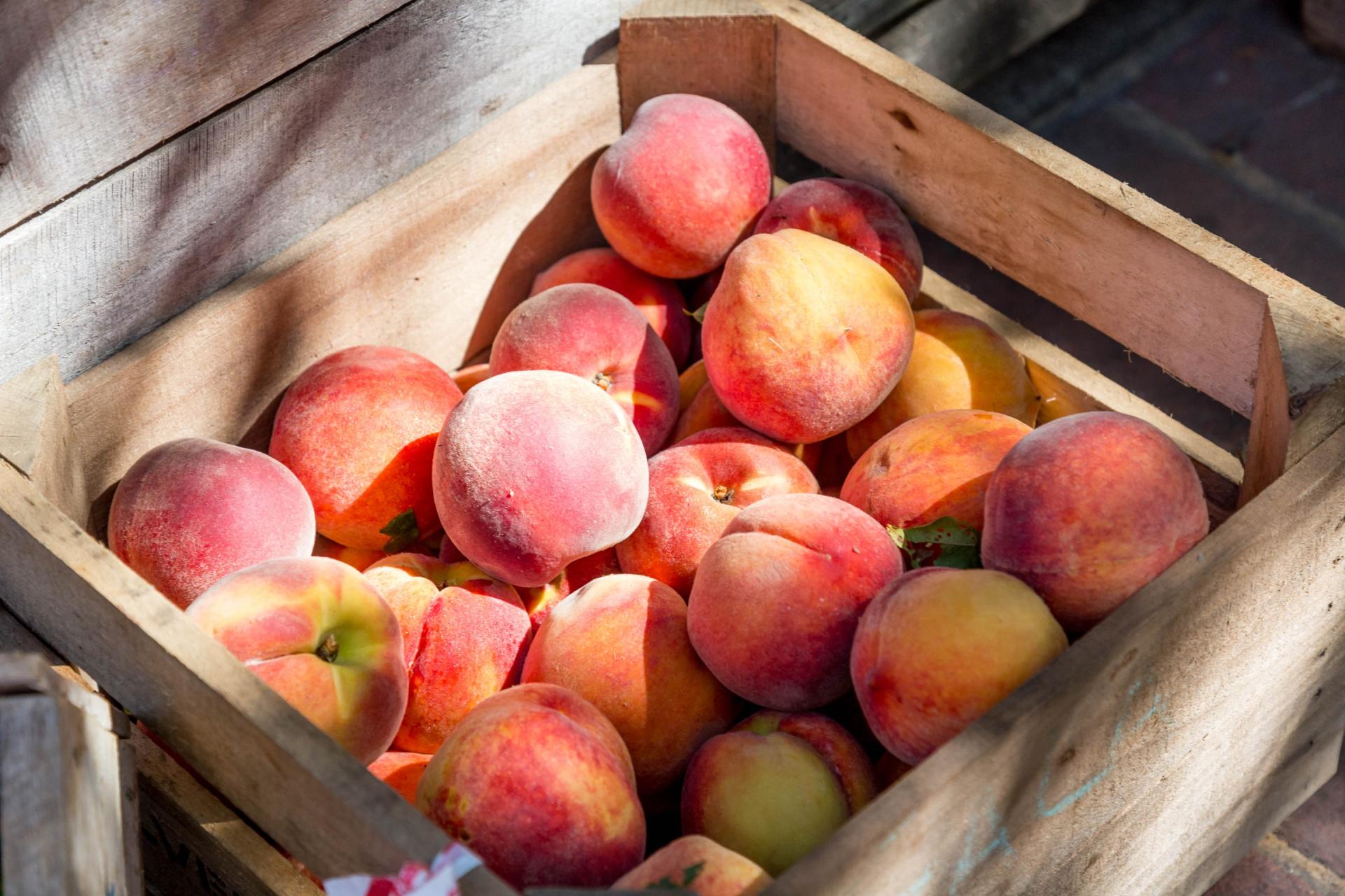 A wooden box filled with peaches is sitting on a table.