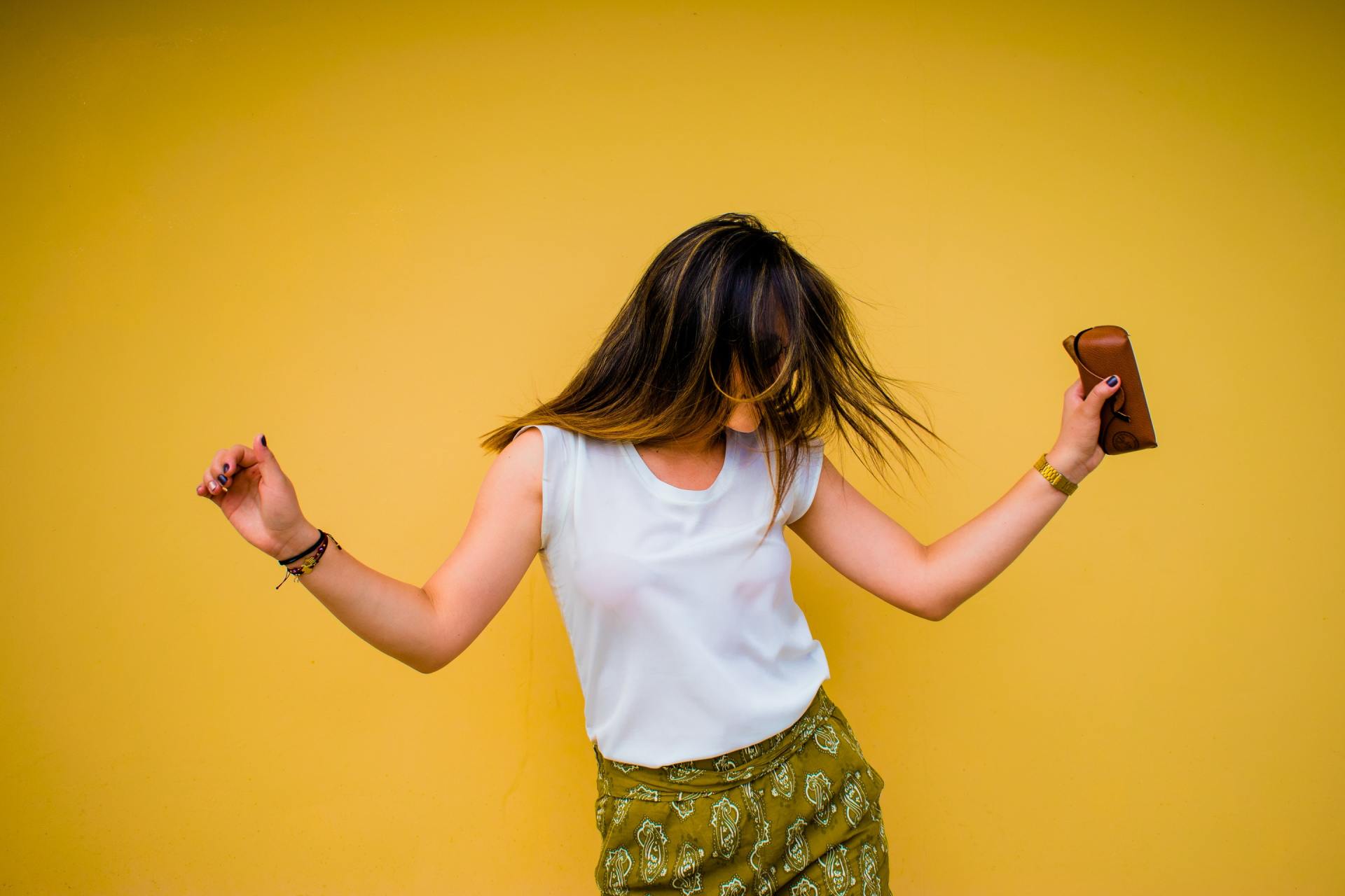 a woman is dancing in front of a yellow wall with her hair blowing in the wind .