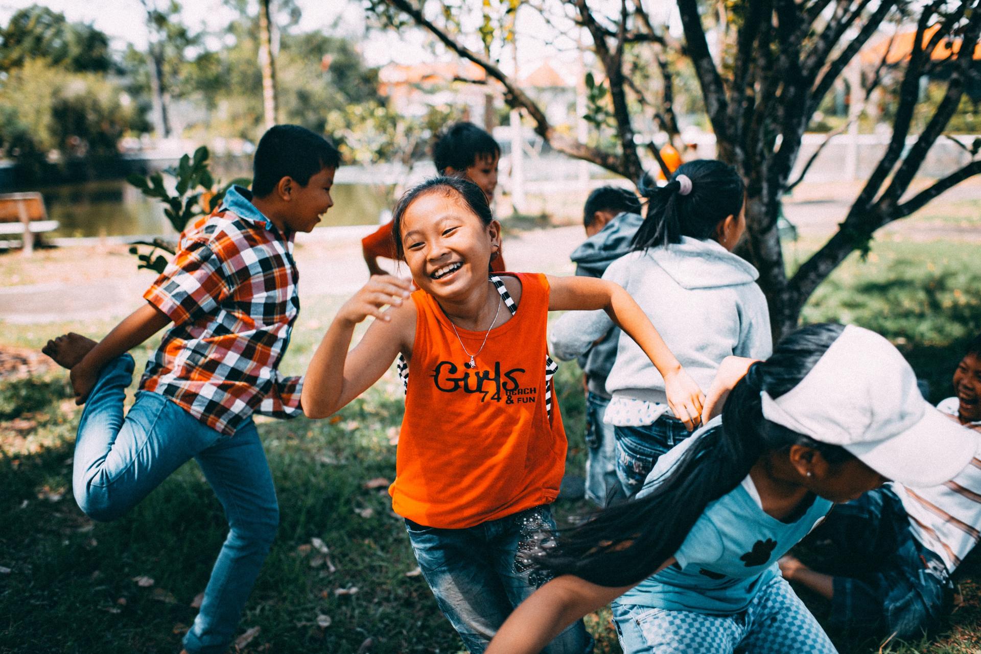 Children playing outdoors, smiling and running in a park with trees.