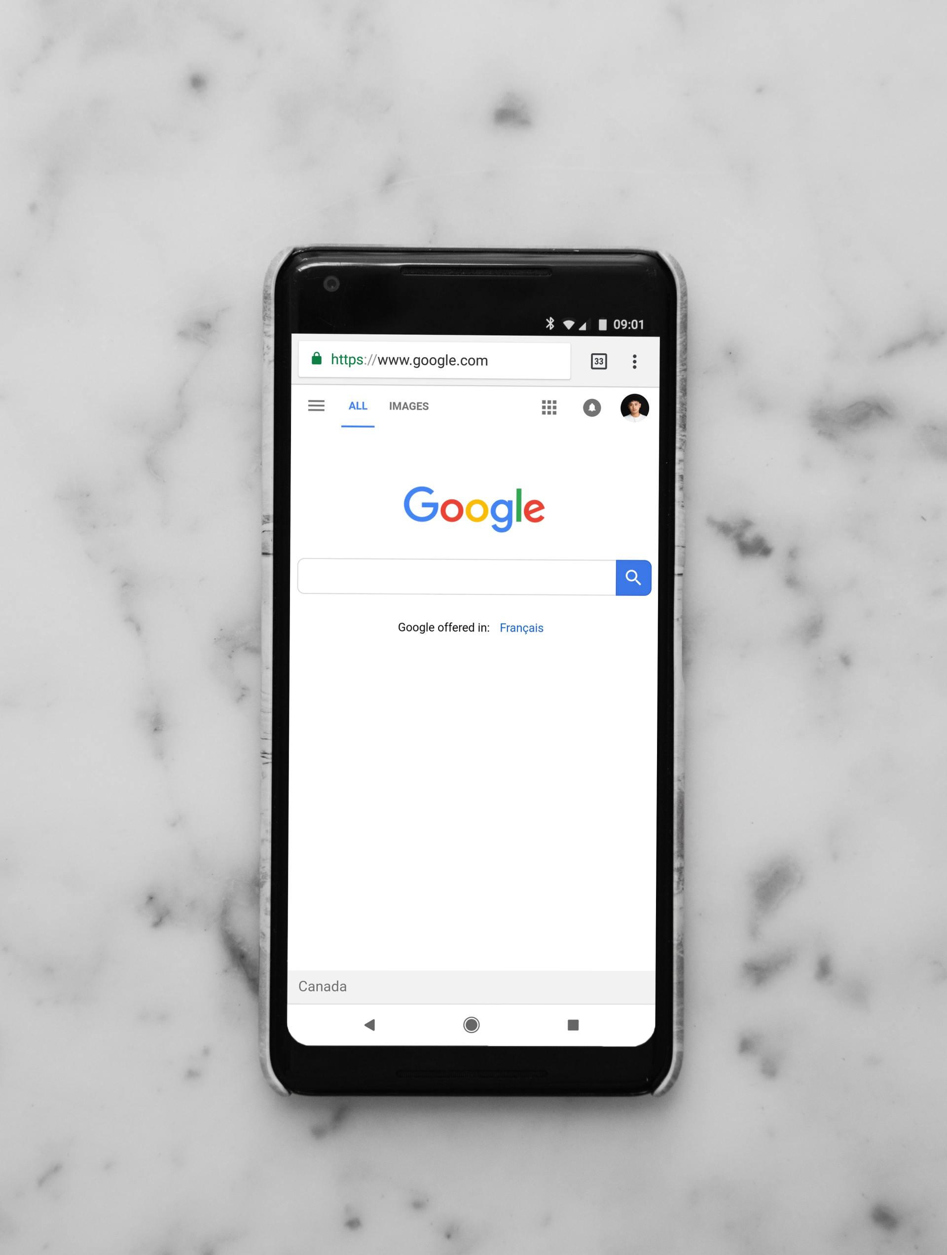 A cell phone is sitting on a marble surface with the google search page open.