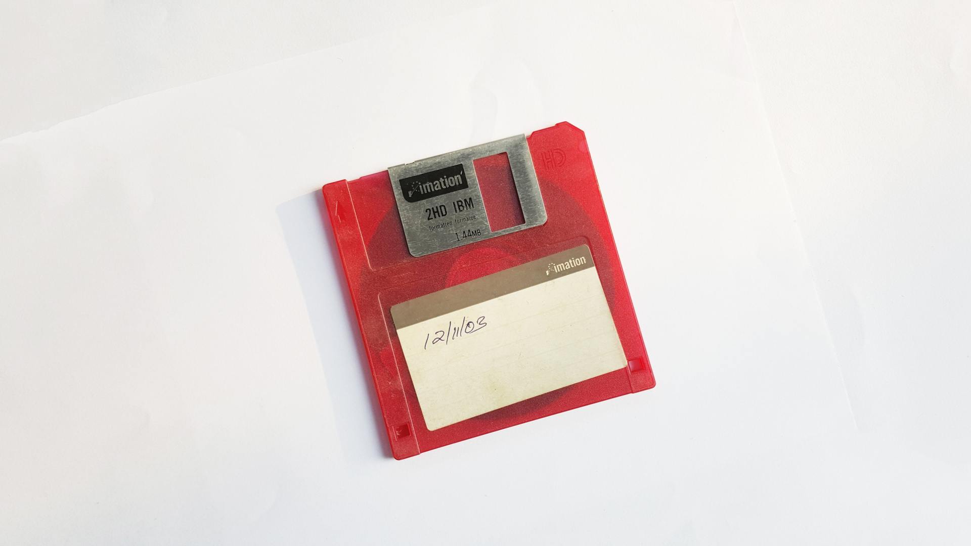A red floppy disk is sitting on a white surface.