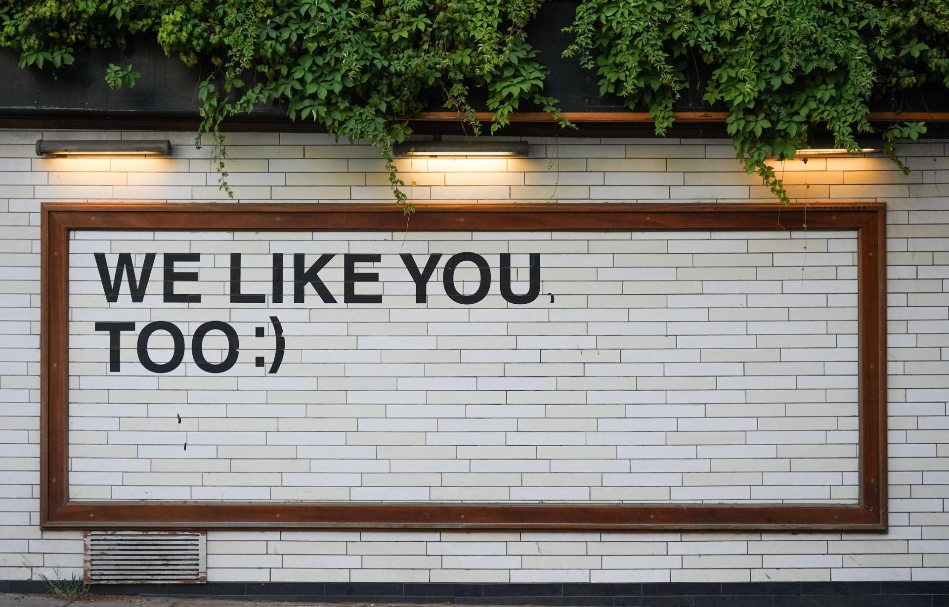 A white brick wall with a sign that says `` we like you too ''.