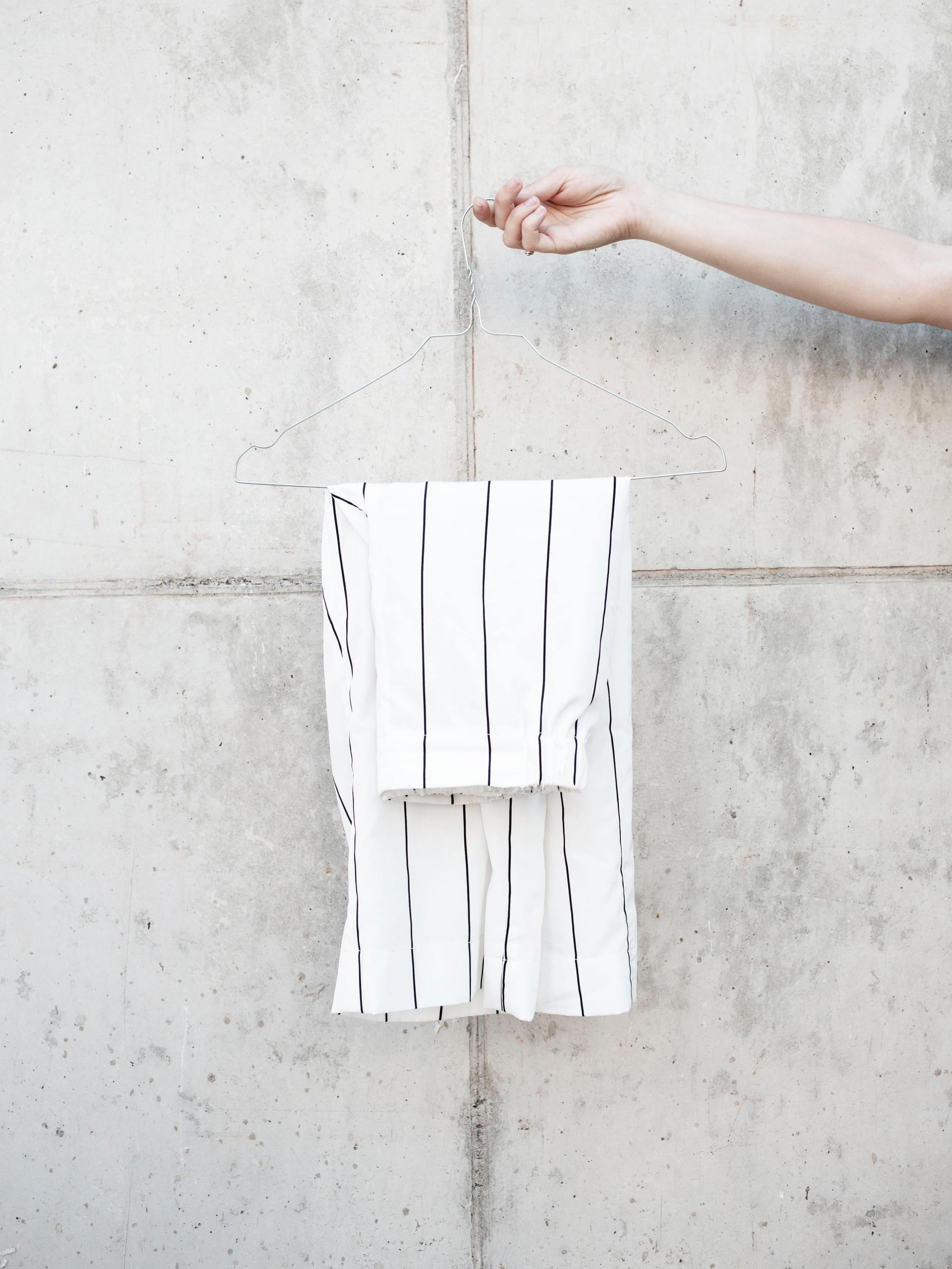 Een witte, gestreepte korte broek hangt aan een betonnen muur, met een hand die er van rechts naar reikt.