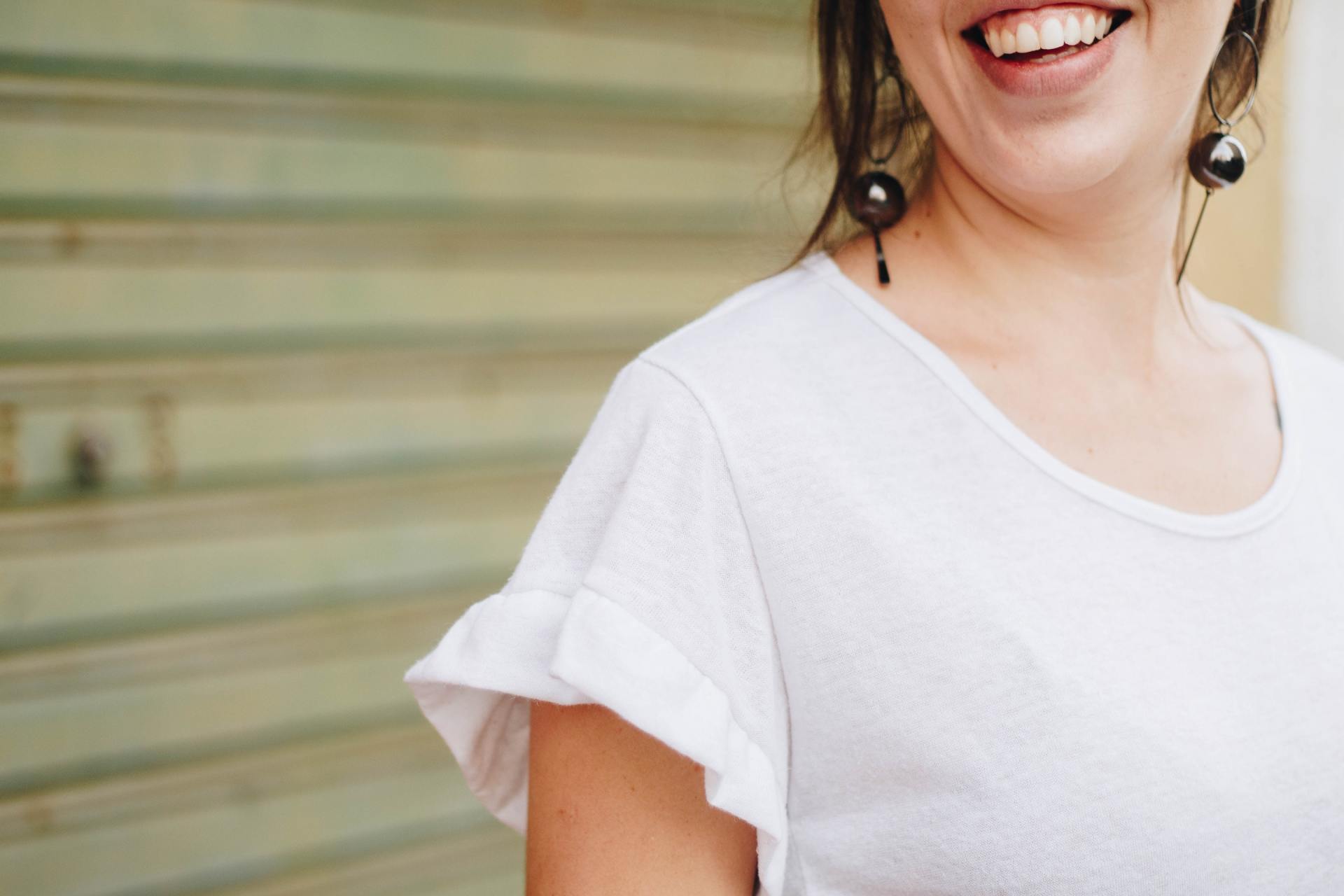 A woman wearing a white t-shirt and earrings is smiling.