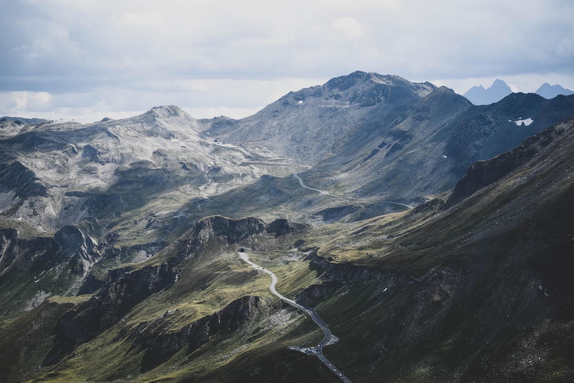 Schneebedeckte Bergkette mit einer kurvenreichen Straße durch ein zerklüftetes Tal unter einem bewölkten Himmel