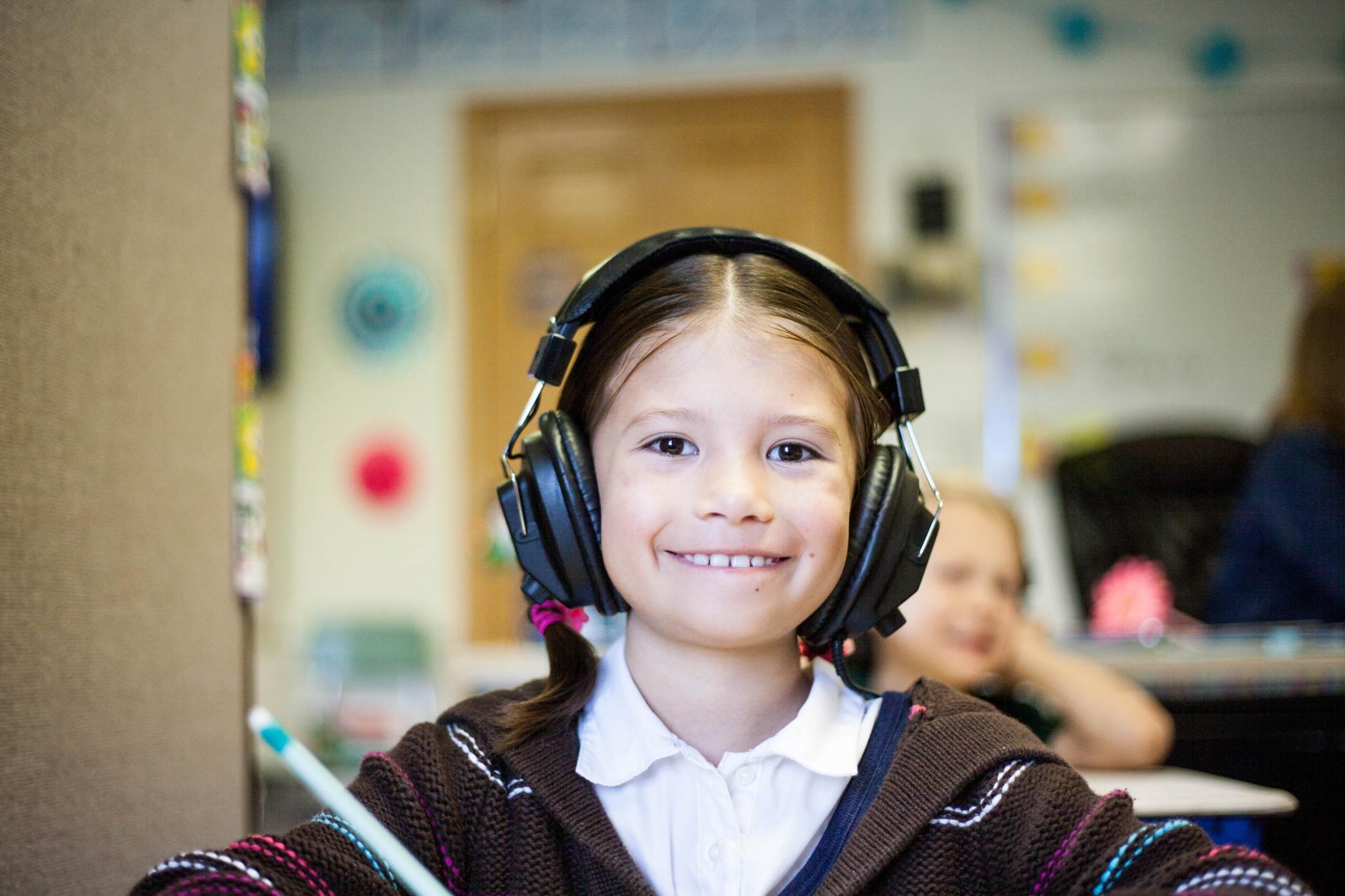 A young girl wearing headphones is sitting at a desk in a classroom.