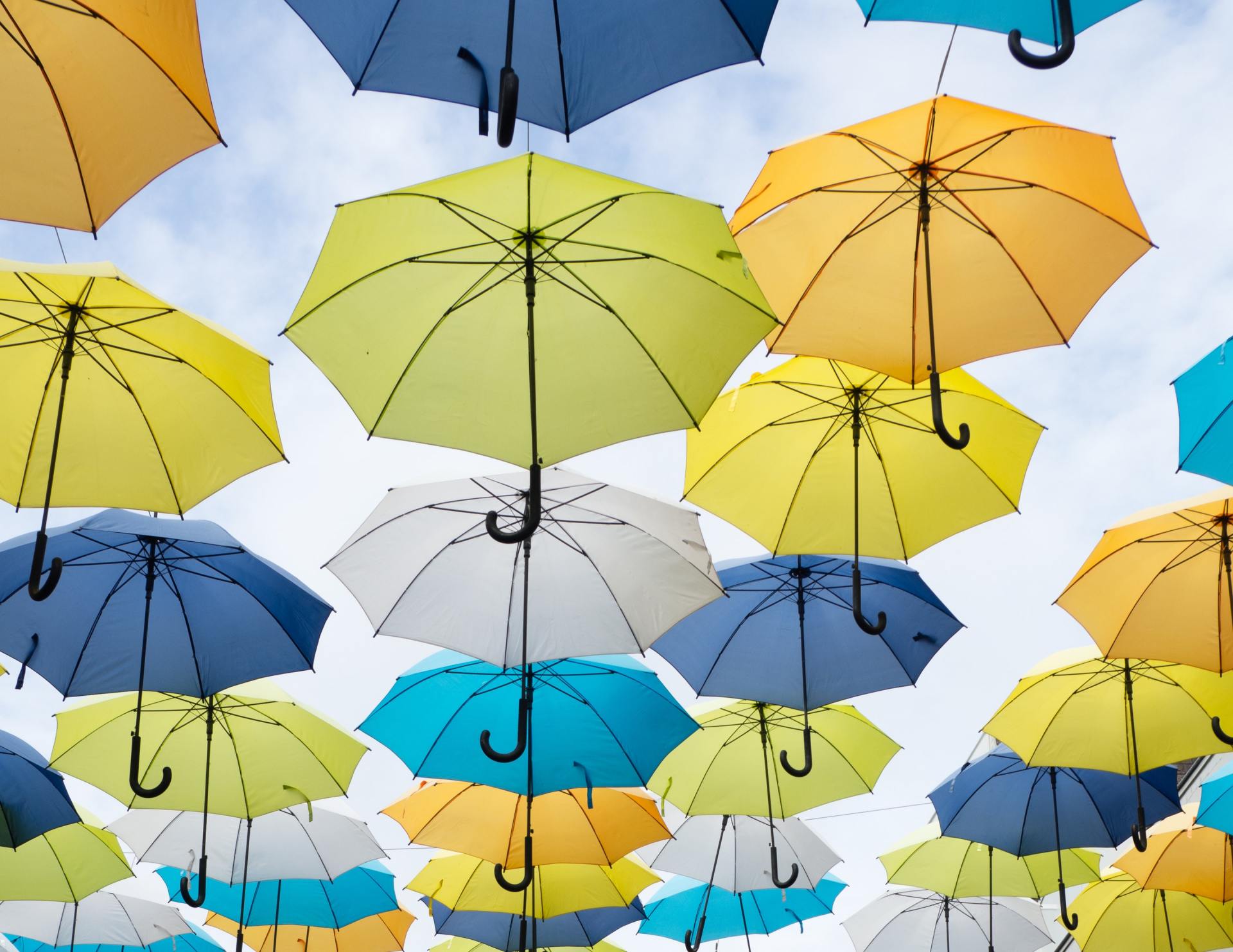 Colorful umbrellas suspended against a cloudy sky. Yellow, blue, and white umbrellas.
