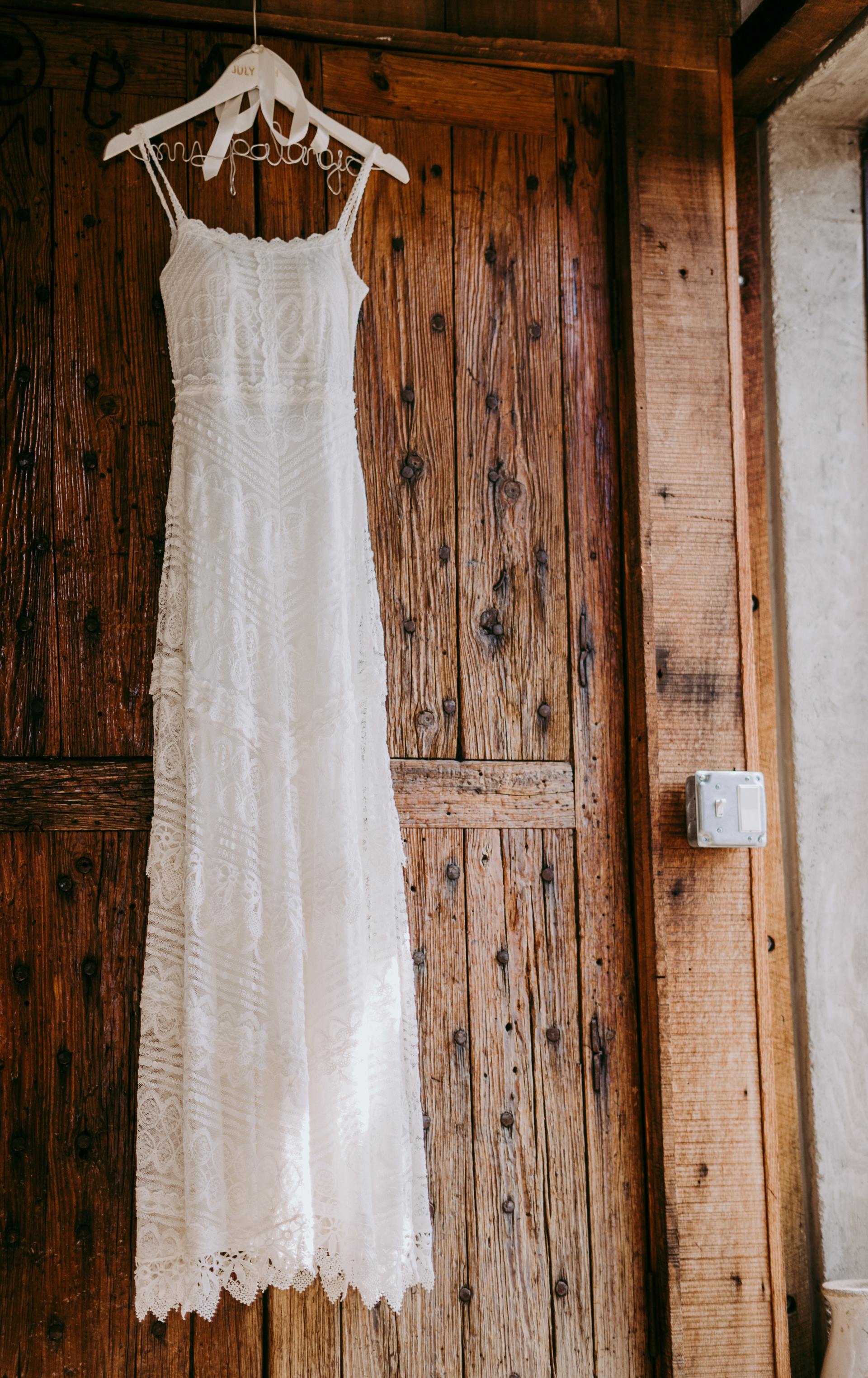 A white lace dress is hanging on a wooden door.