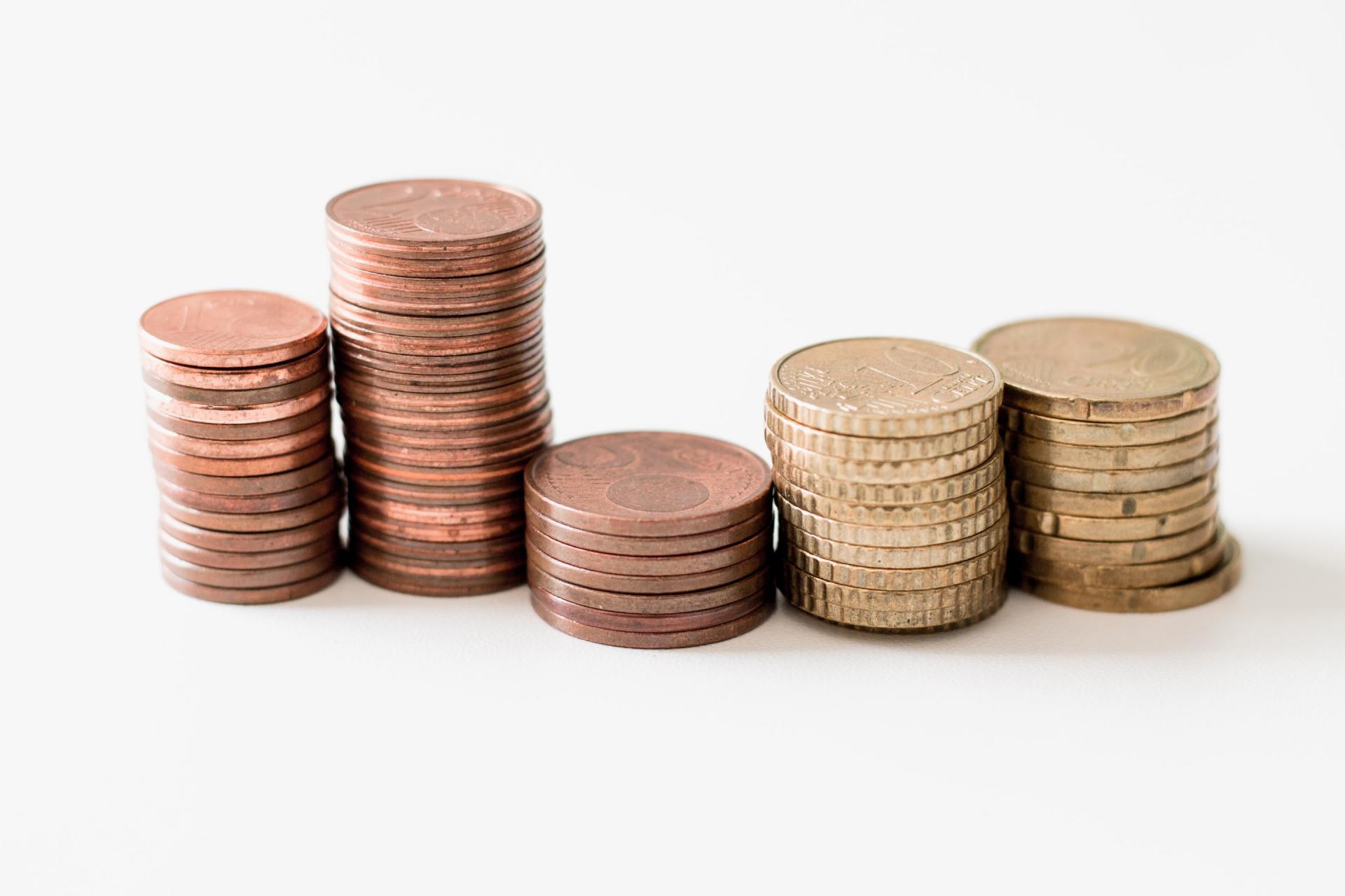 Five stacks of coins on a white surface. Three stacks are copper-colored, and two are gold-colored.