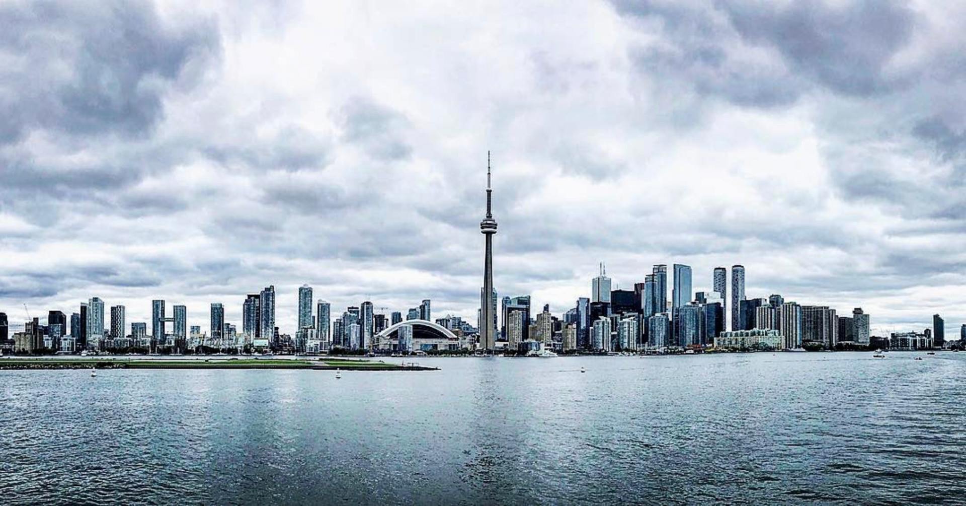 A city skyline is visible over a body of water on a cloudy day.
