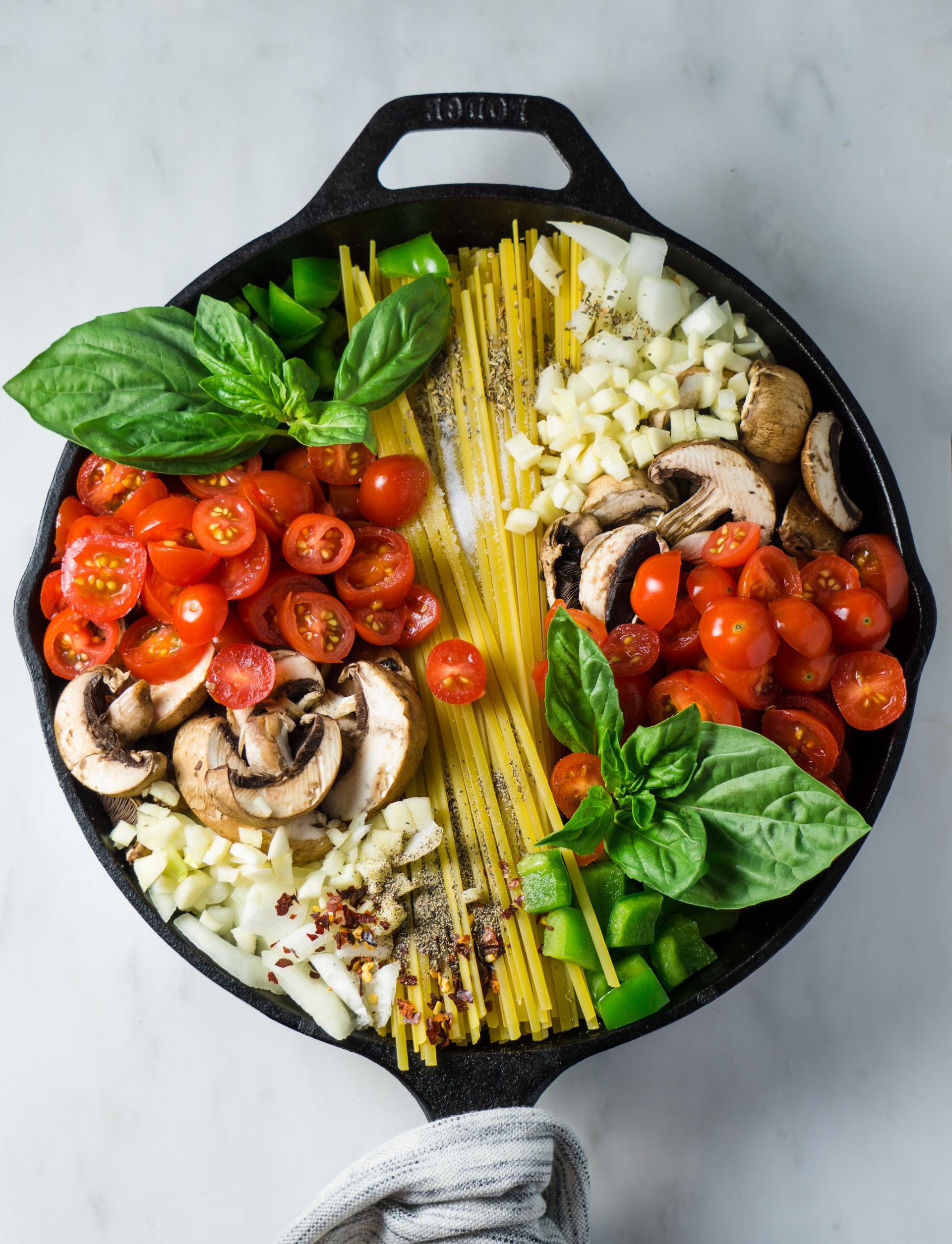 A skillet filled with spaghetti , tomatoes , mushrooms , basil and cheese.