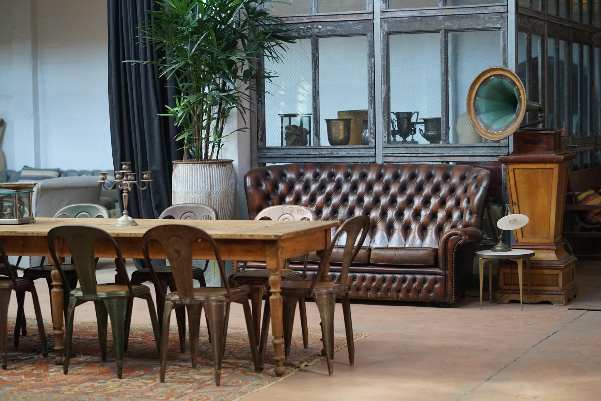 Rustic dining room with a long table, metal chairs, leather sofa, and vintage gramophone.