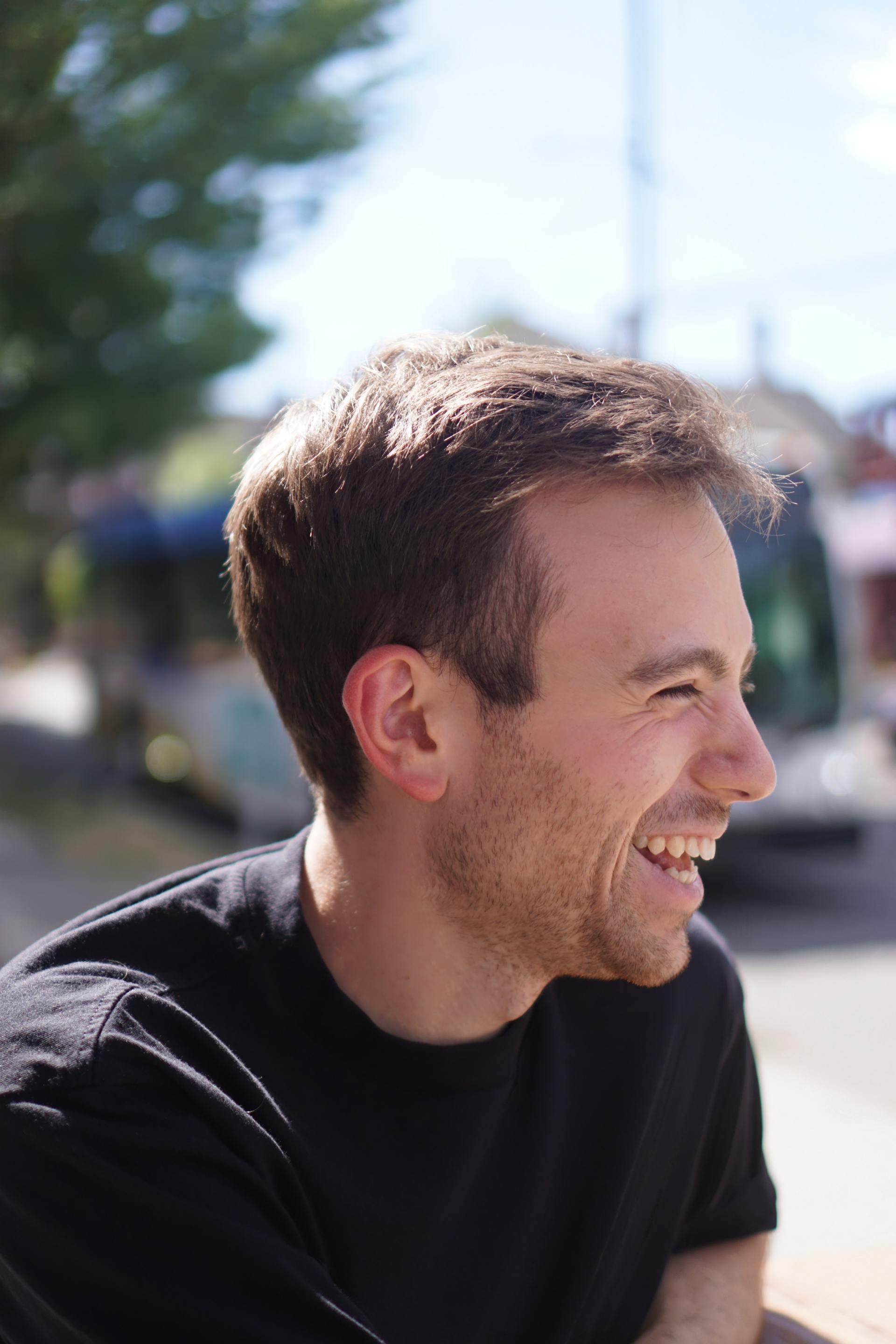 A man in a black shirt is smiling with a bus in the background