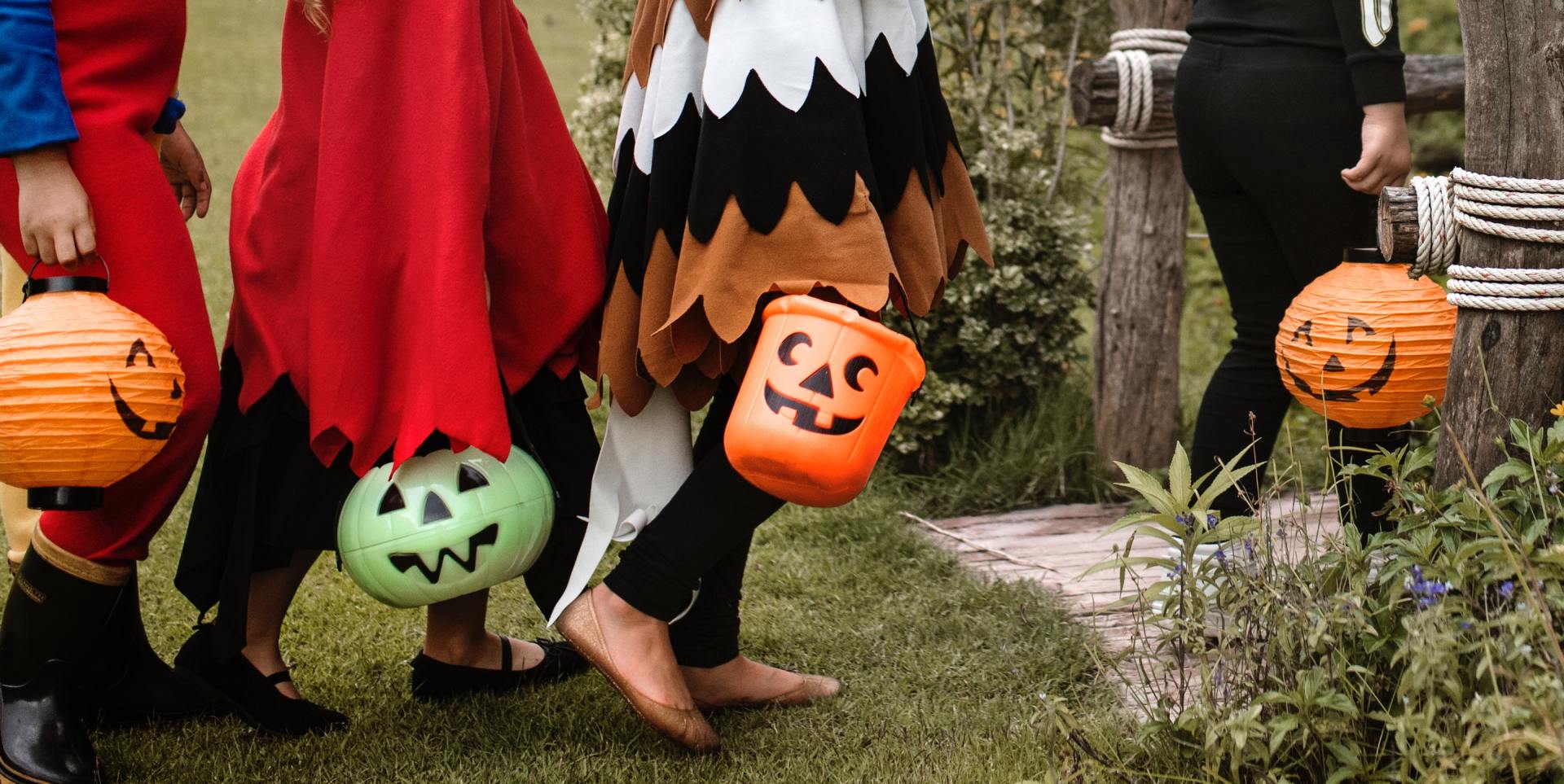 A group of children in halloween costumes are walking down a path carrying trick or treat buckets.