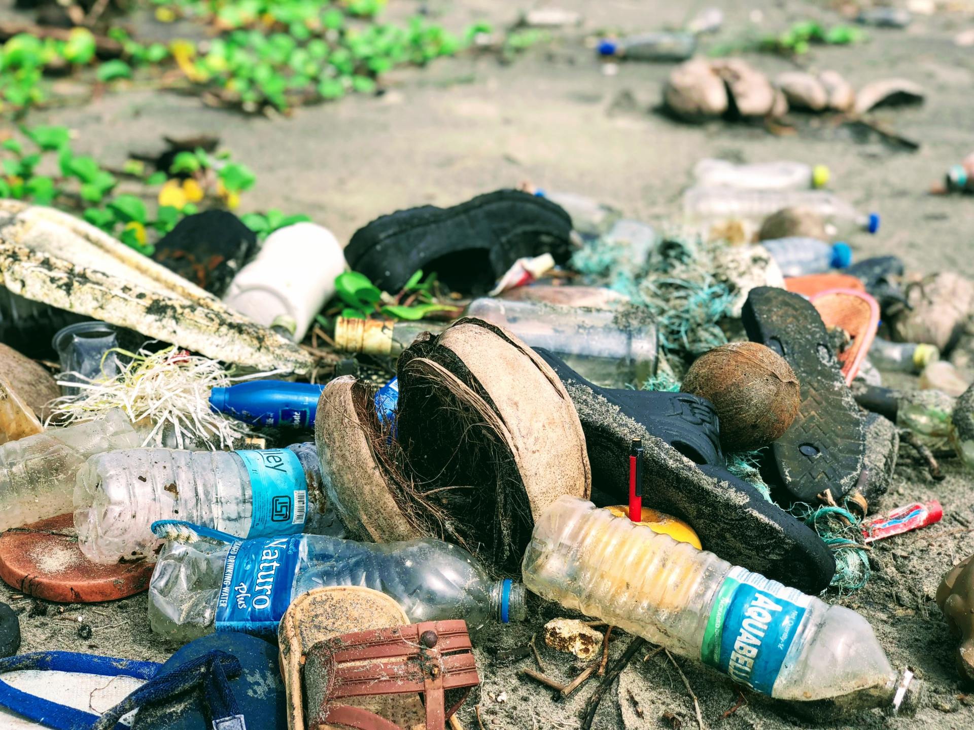 A pile of plastic bottles , flip flops , and other trash on a beach.