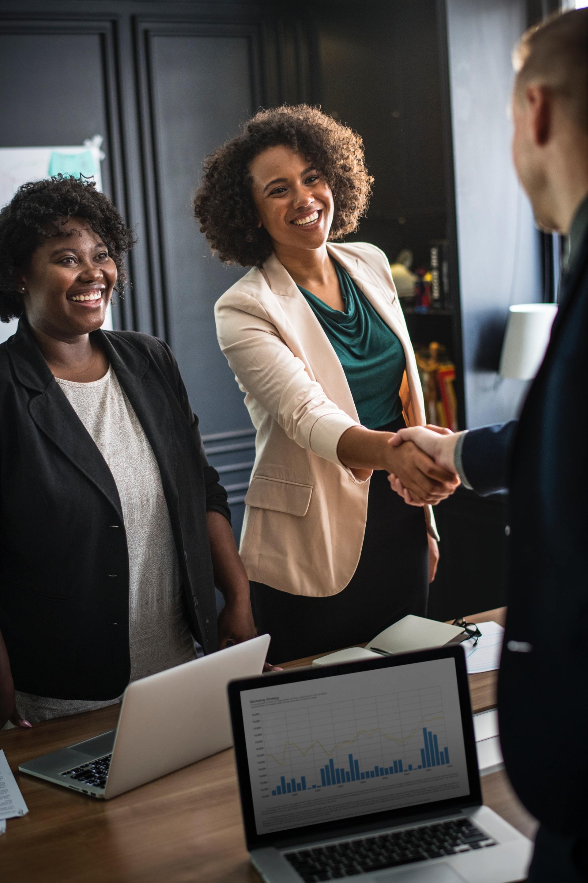 Two women are shaking hands with a man in an office.