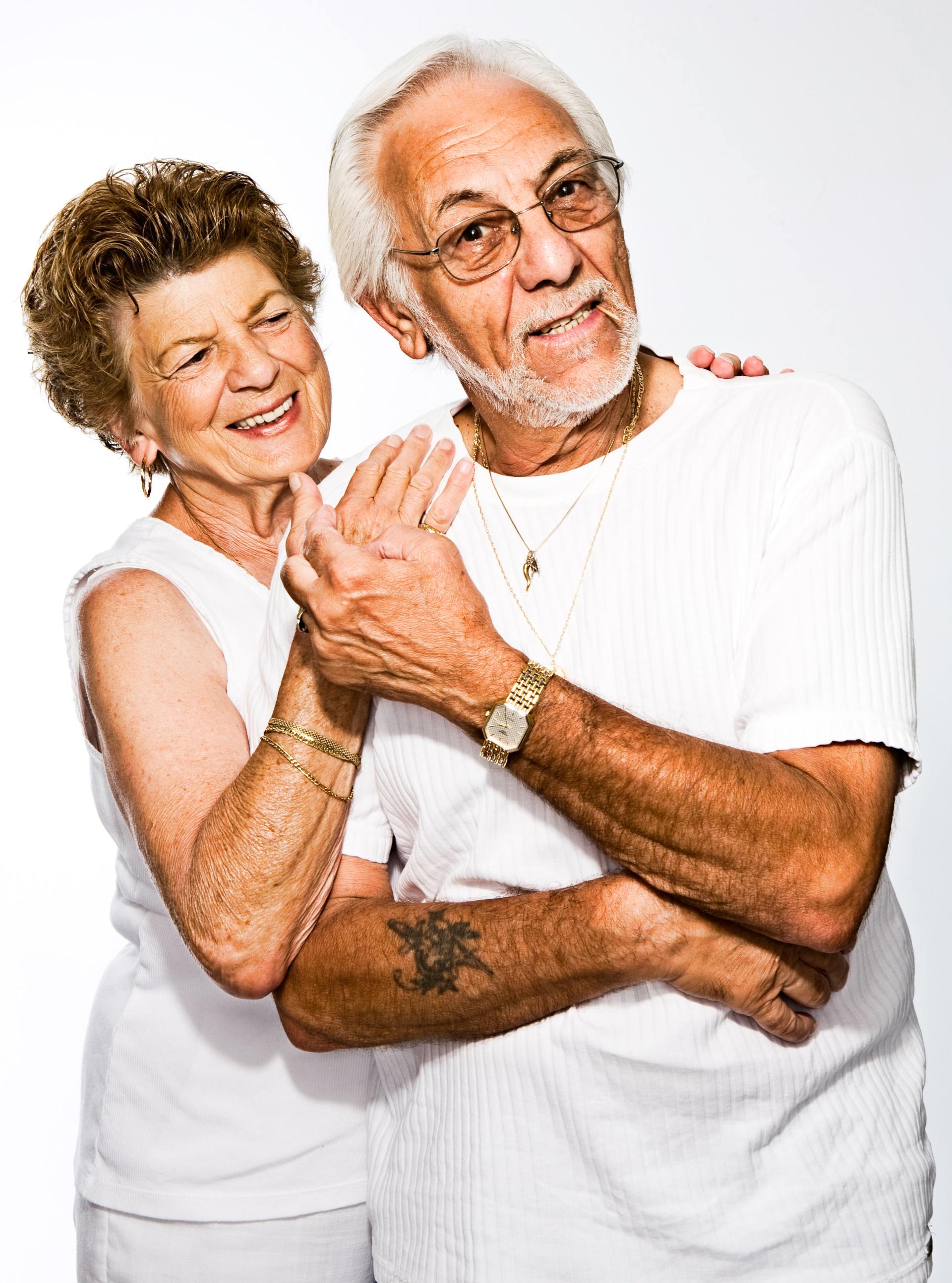 An elderly couple standing next to each other with their arms crossed