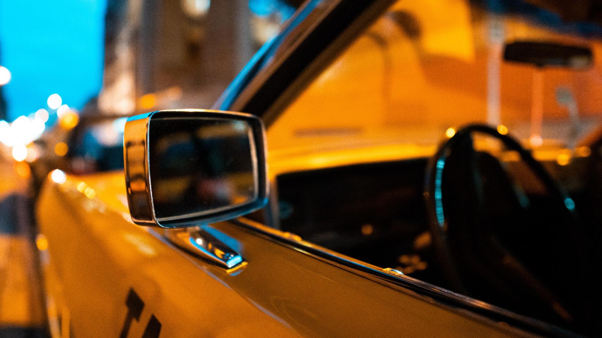 Yellow classic car with side mirror and interior visible, city street at night, with streetlights.