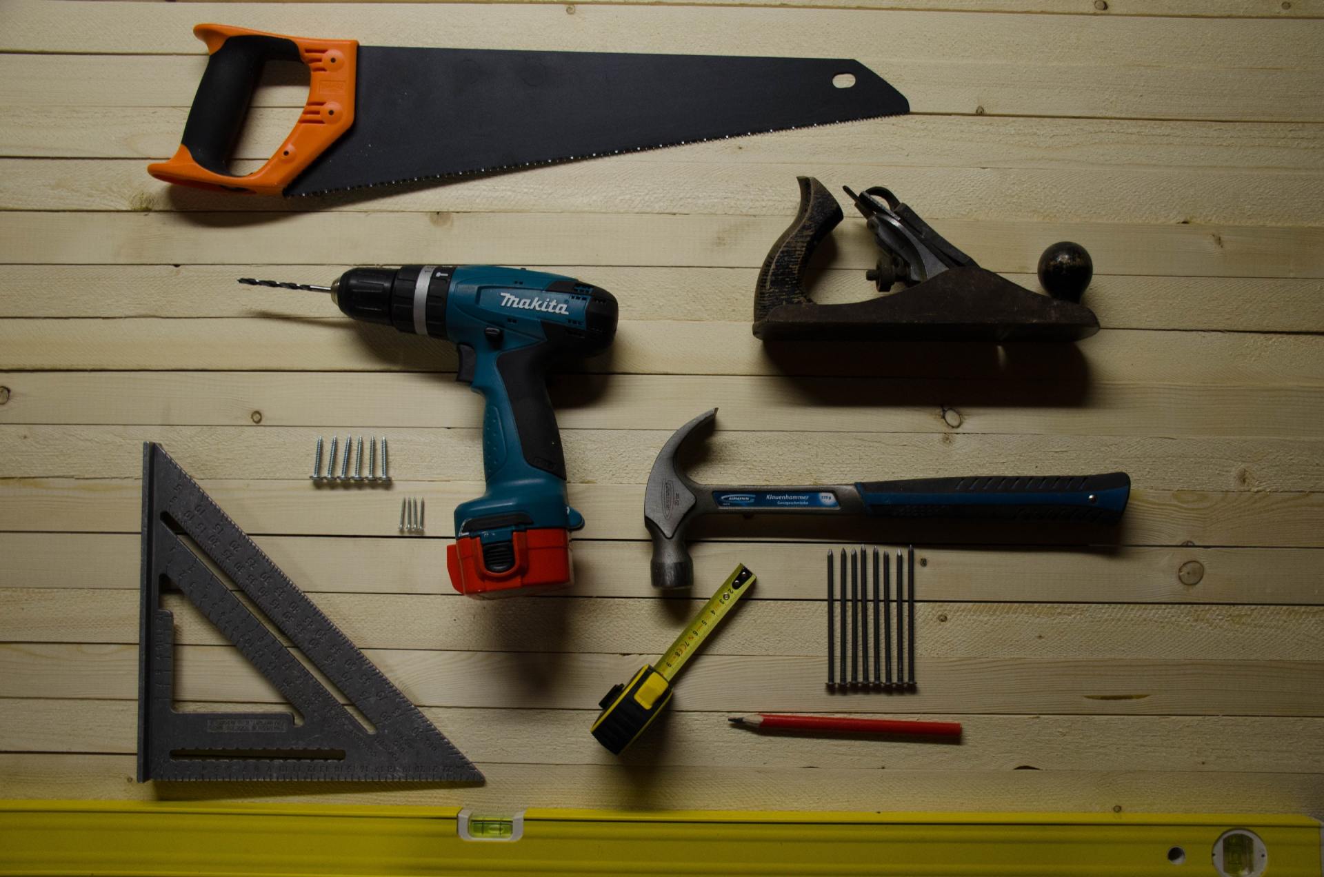 A wooden table topped with a drill , hammer , ruler , and other tools.