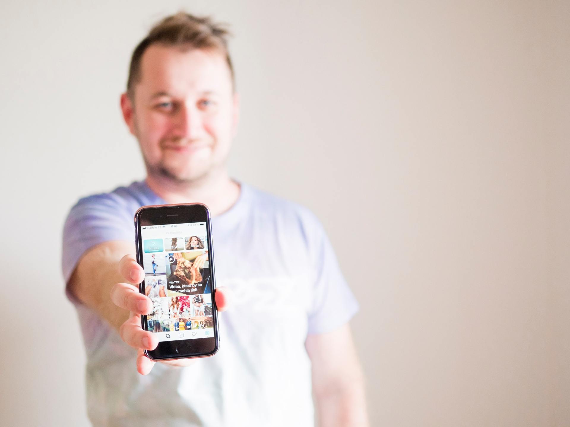 Man holding out a smartphone with a display of photos against a light background.