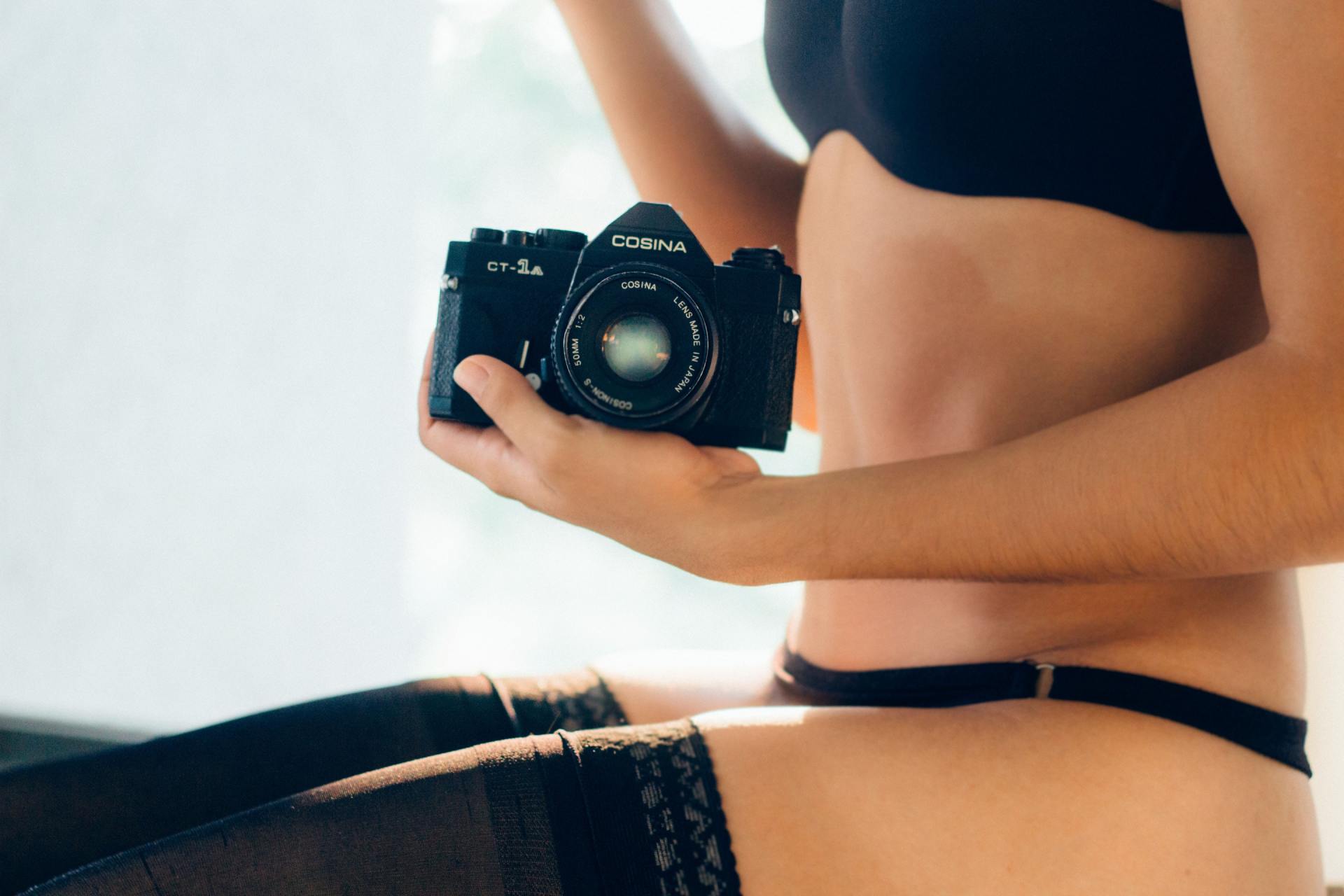 A woman in lingerie is holding a camera in her hand.