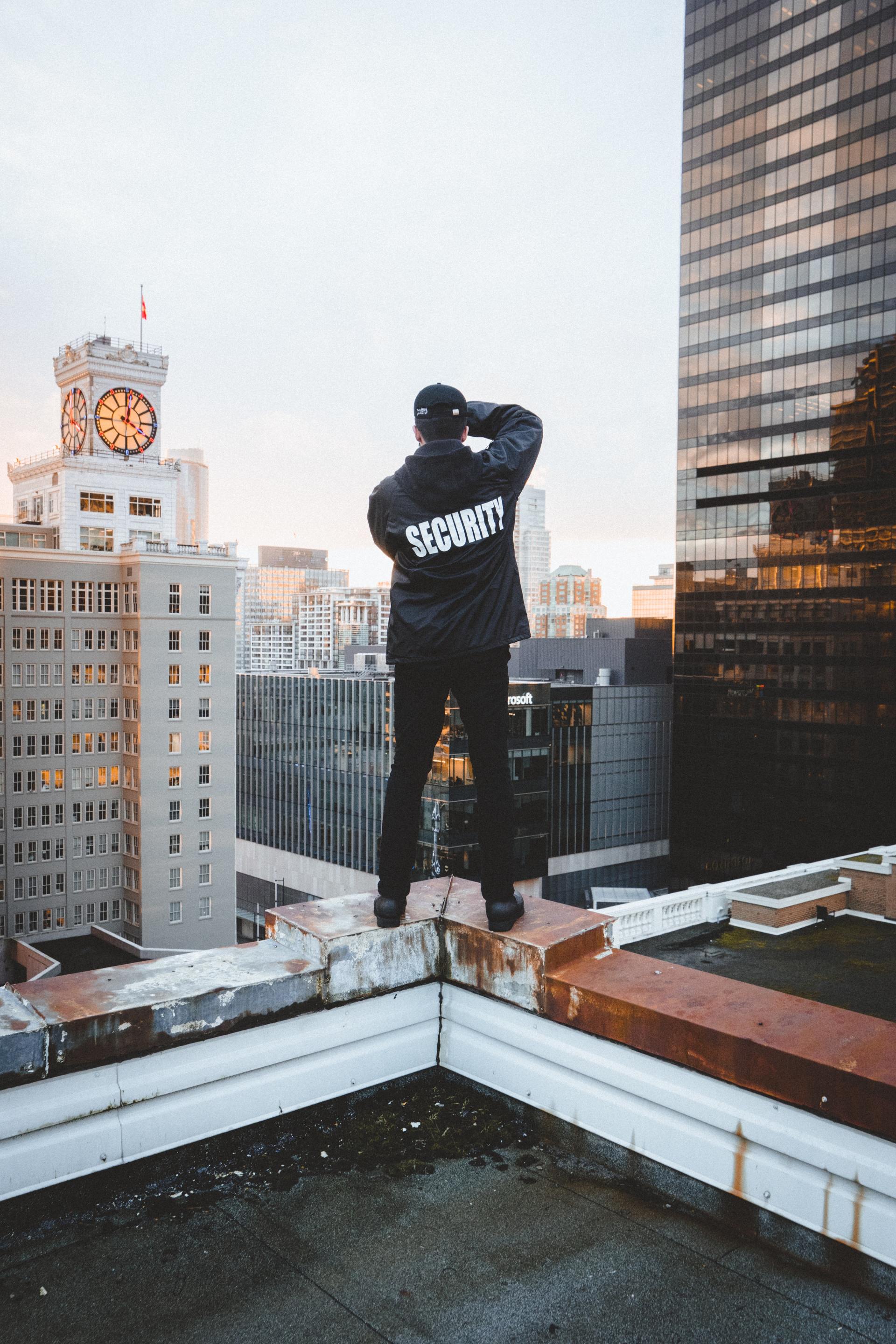 Person in black hoodie stands on a rooftop, looking over a city skyline at dusk.