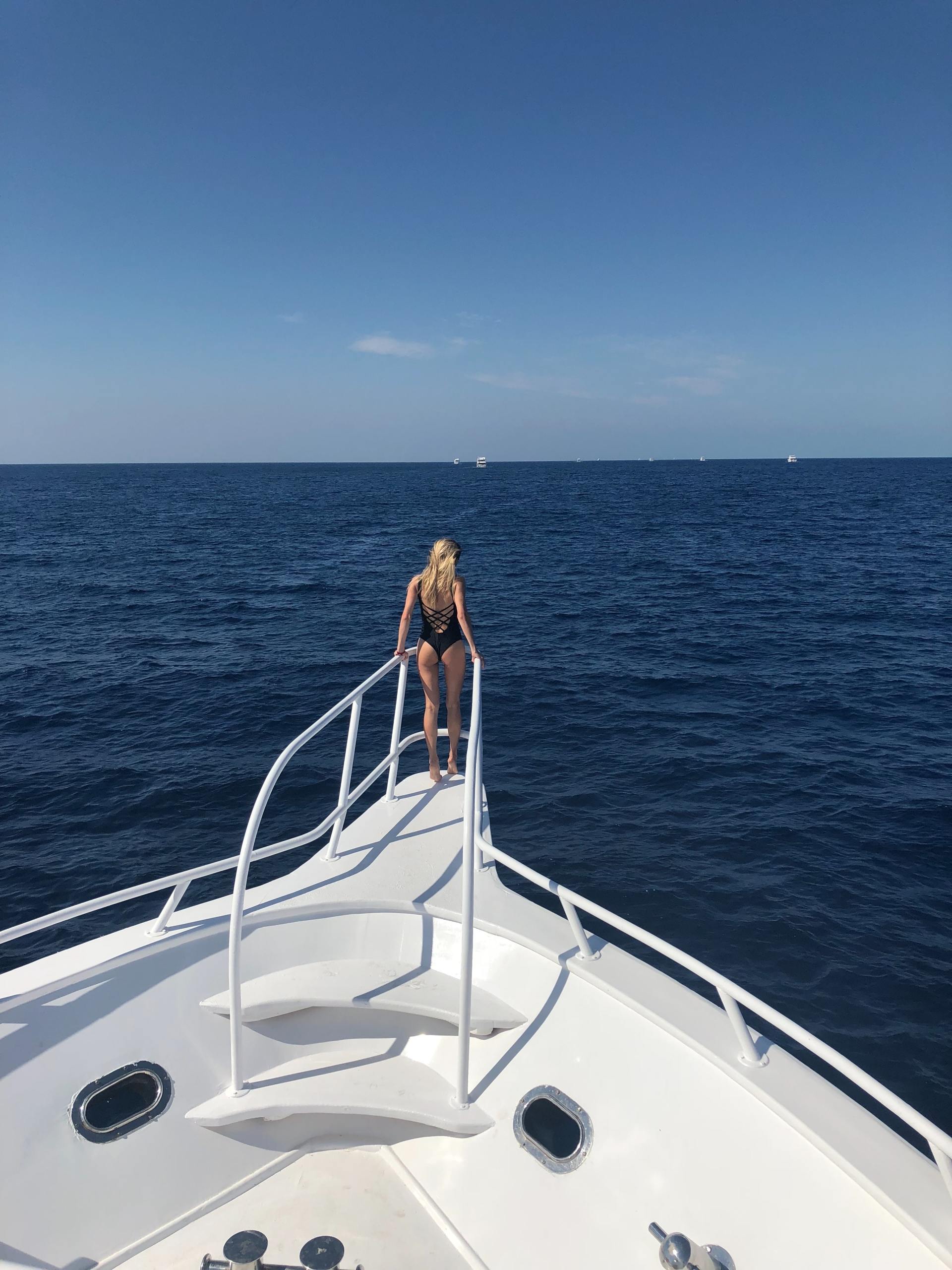 A woman in a bathing suit is standing on the back of a boat in the ocean