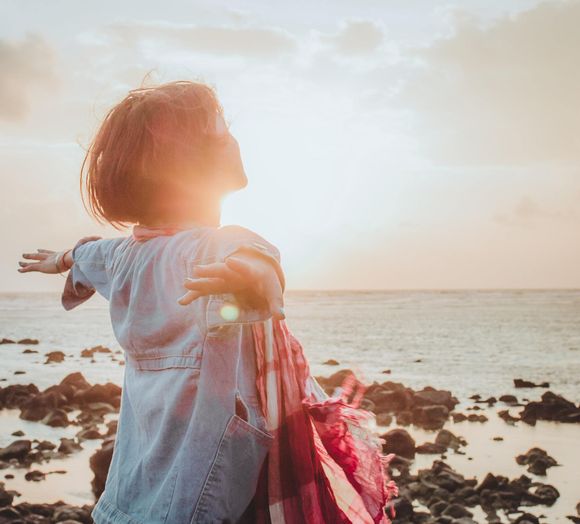Vrouw met uitgestrekte armen boven de oceaan, gezicht naar de zon