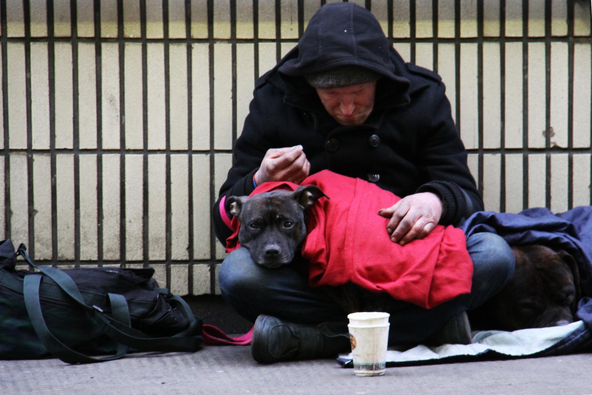 unhoused man huddles with his dog on his lap