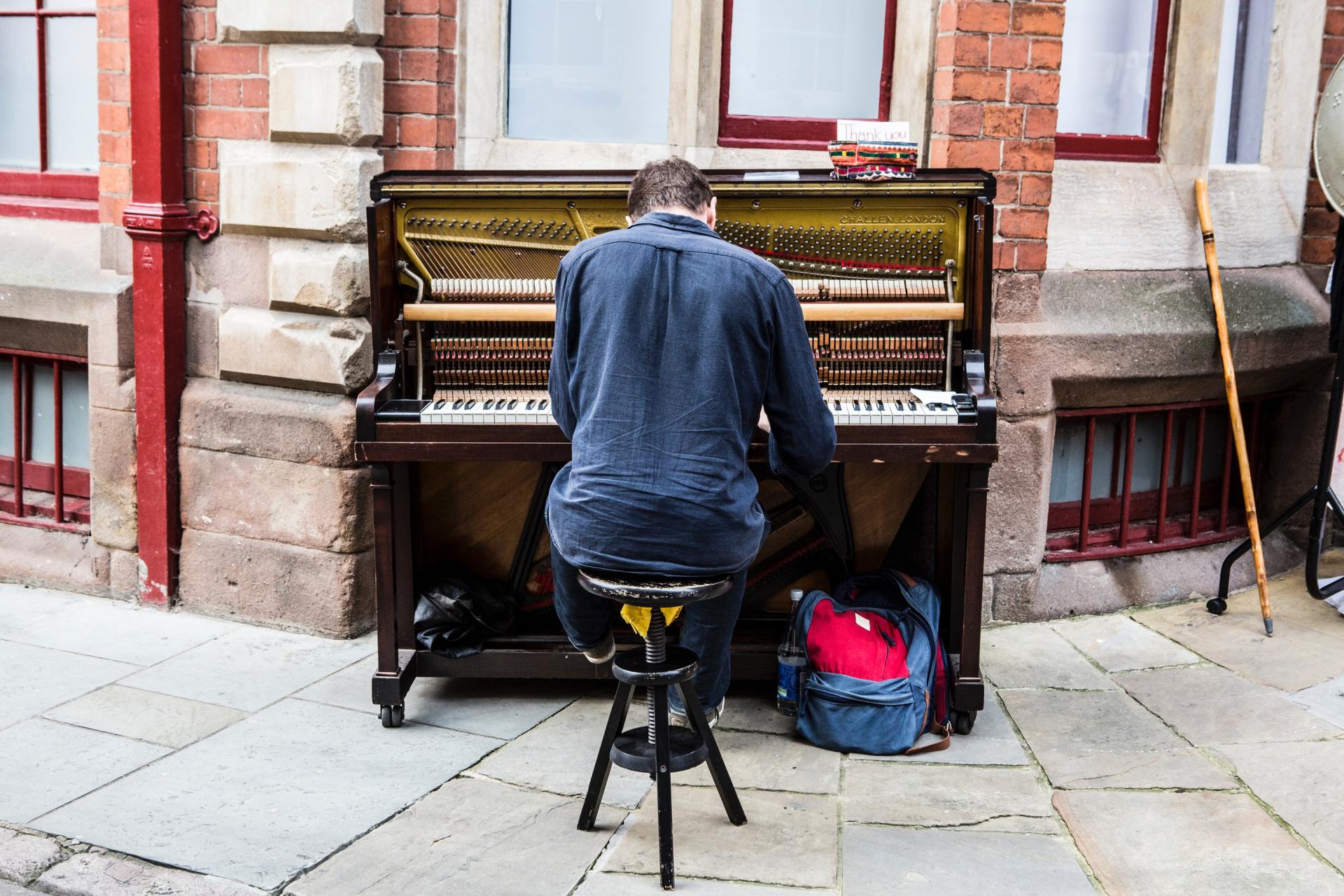A man is sitting on a stool playing a piano on the sidewalk.