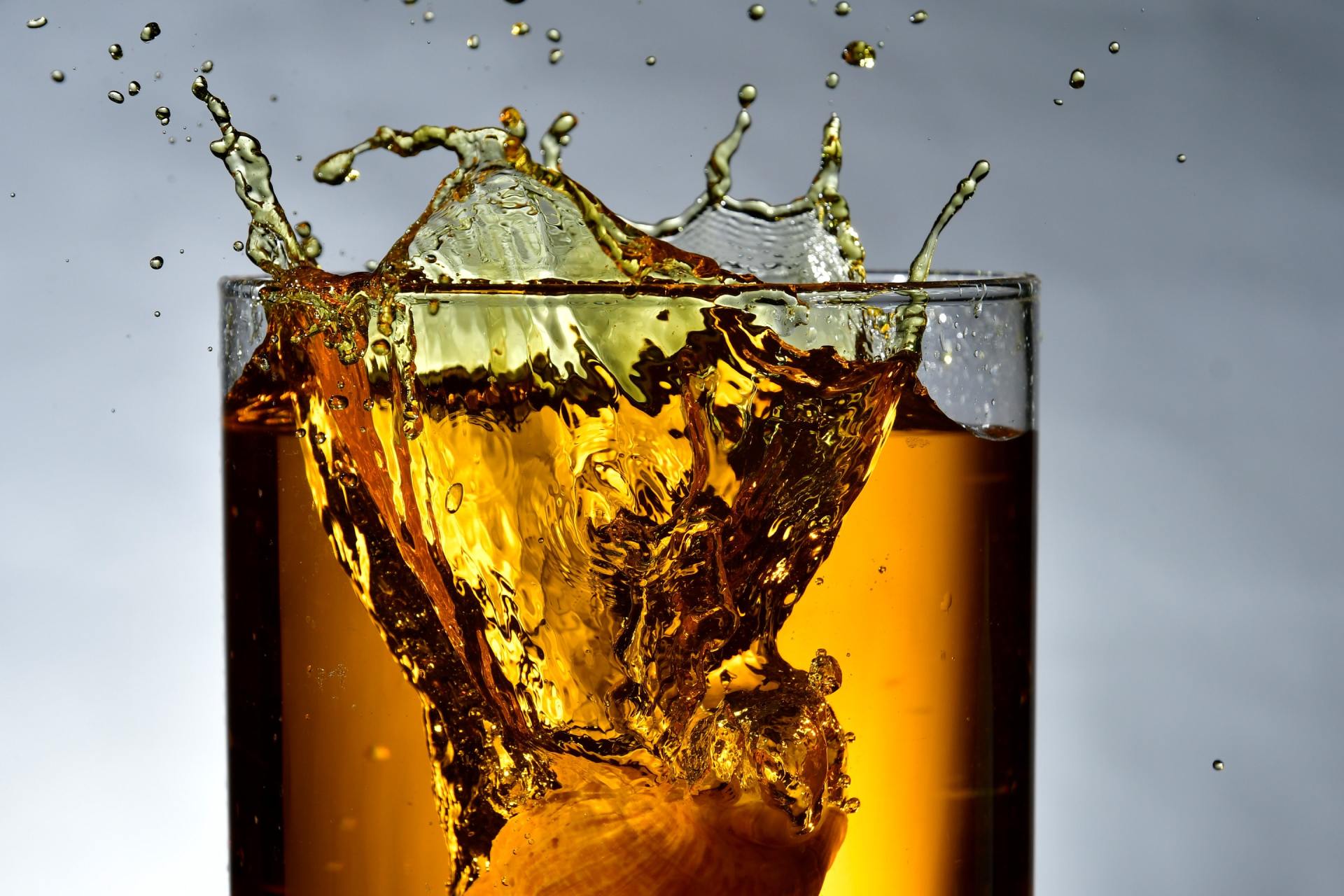 A glass of whiskey with ice cubes splashing out of it