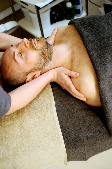 Man lying on a couch while a hand gently supports his neck during a massage.
