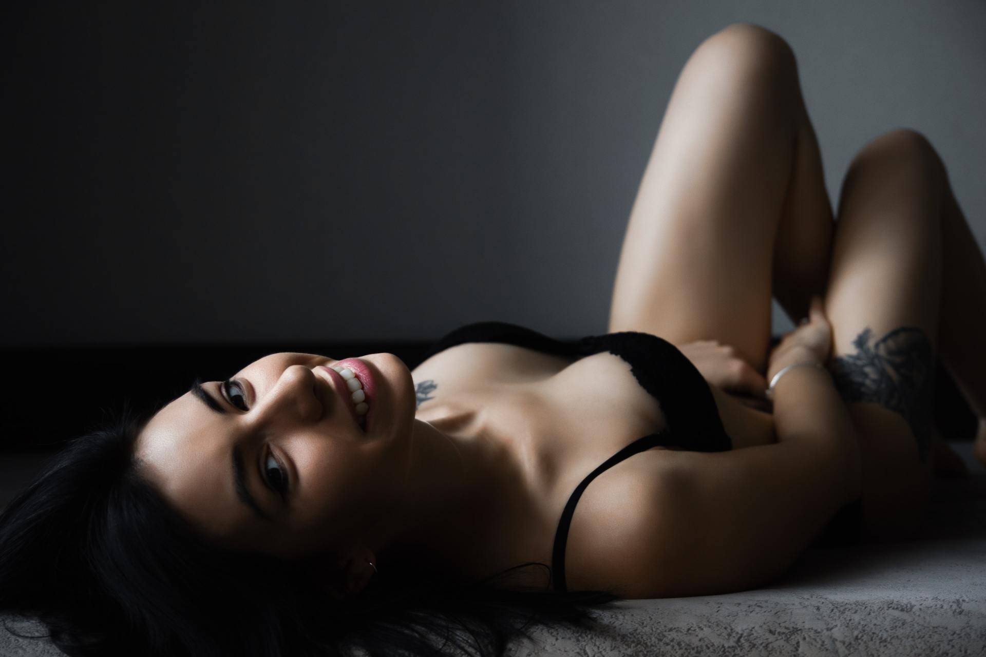 A woman in lingerie is laying on the floor and smiling.