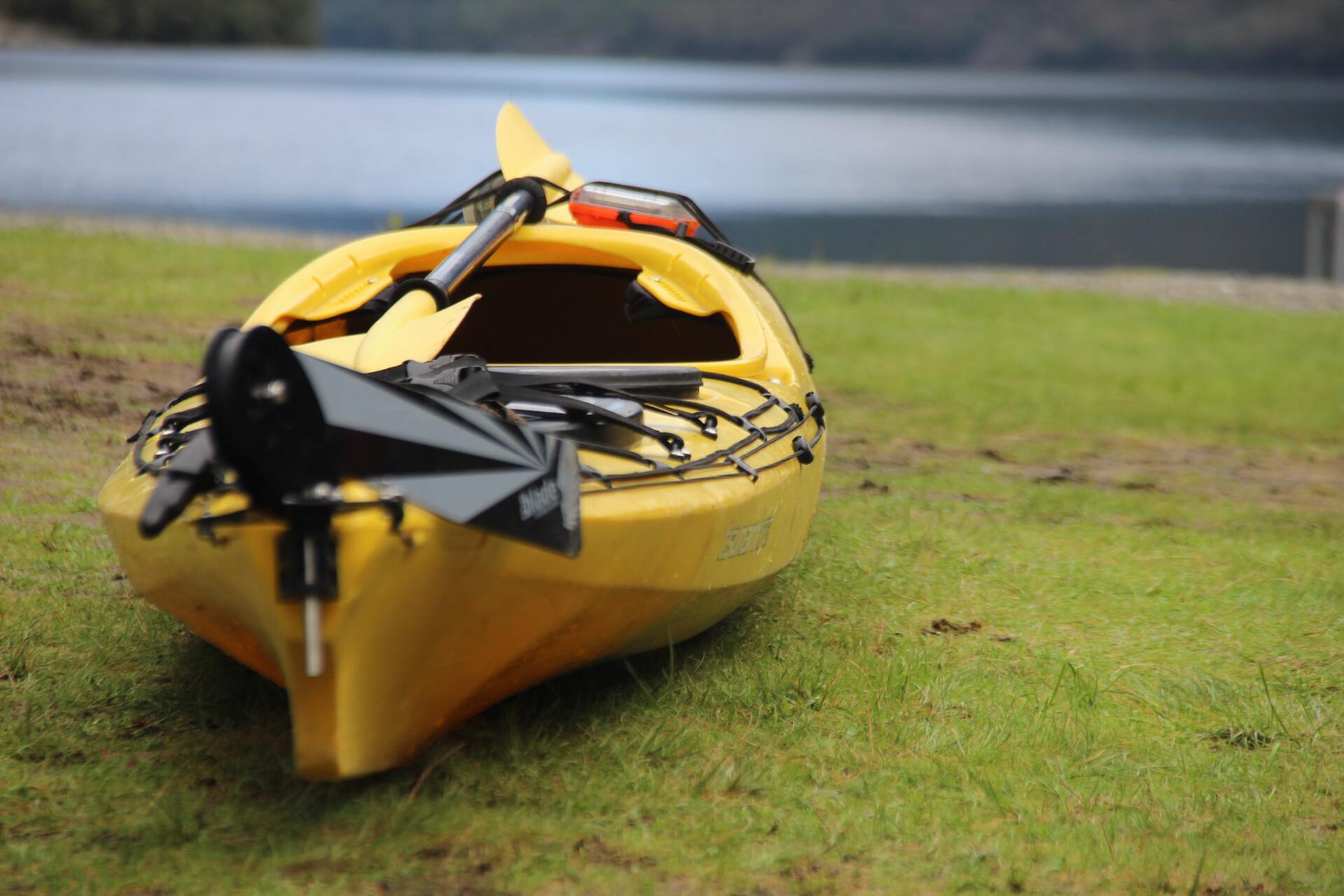 Yellow kayak on green grass next to a body of water with an overcast sky.